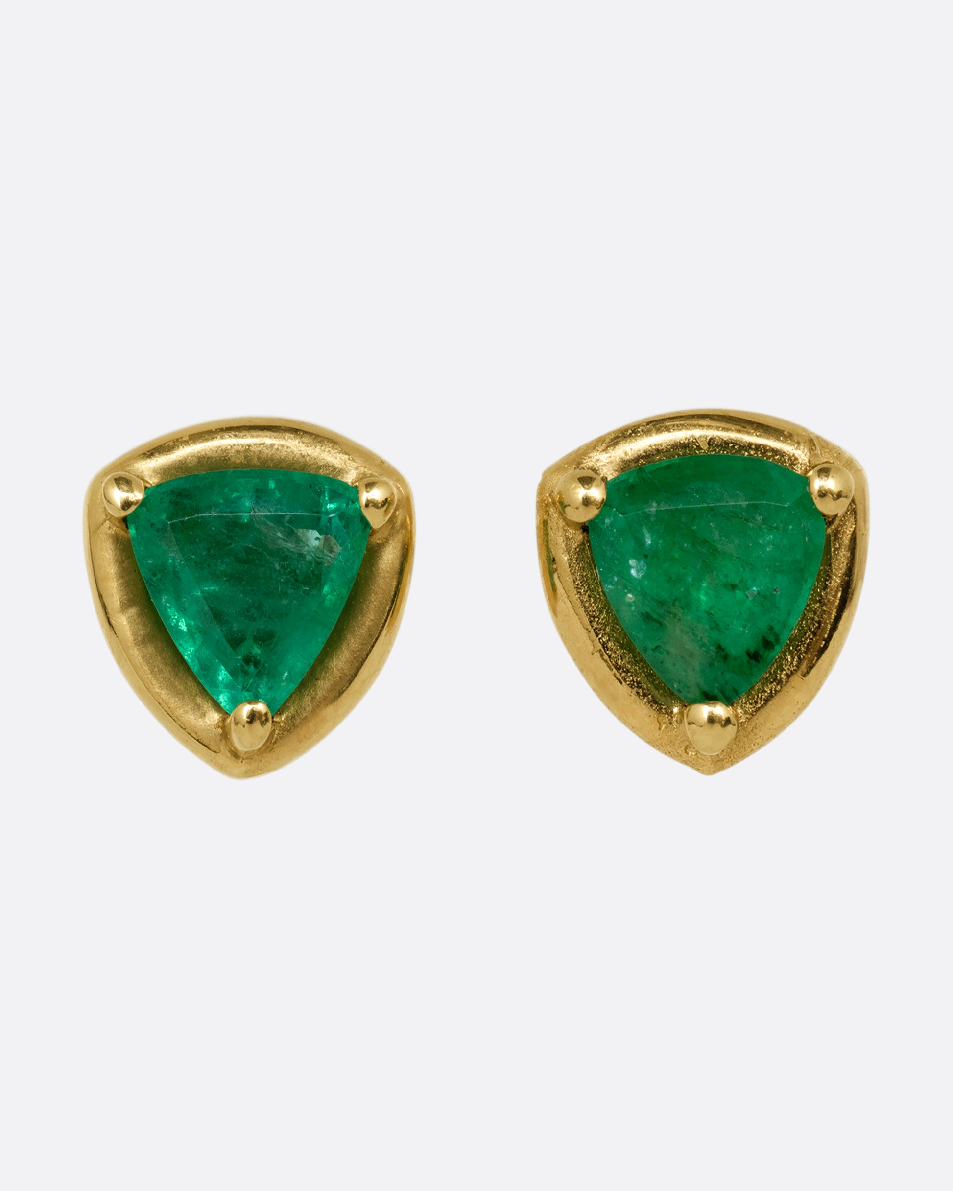 A pair of yellow gold stud earrings with emeralds. Shown from the front.