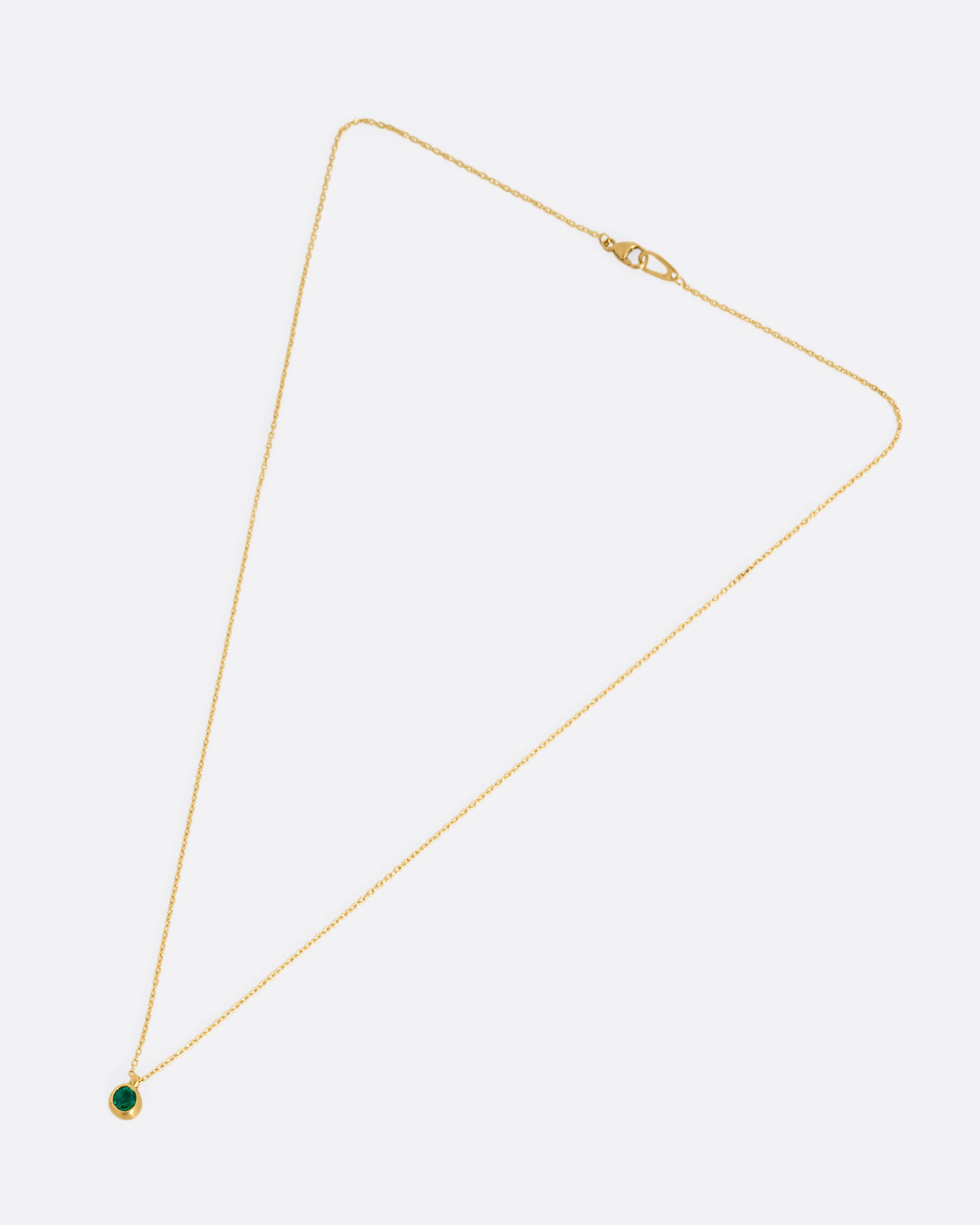 A yellow gold cable chain necklace with a faceted emerald in a satiny gold bezel. Shown clasped lying flat from the front.