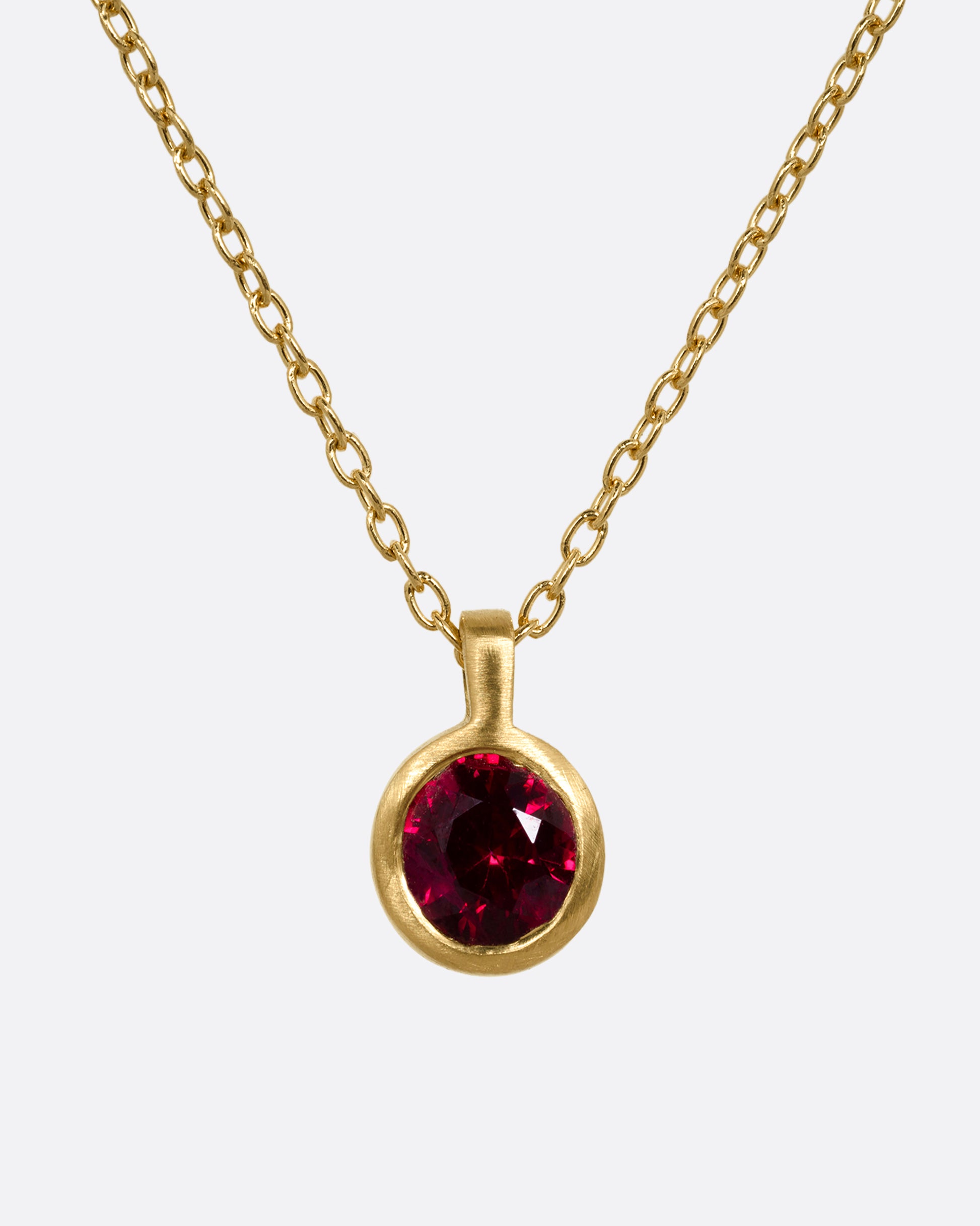 A yellow gold cable chain necklace with a single round ruby in a brushed gold bezel. Shown from the front.