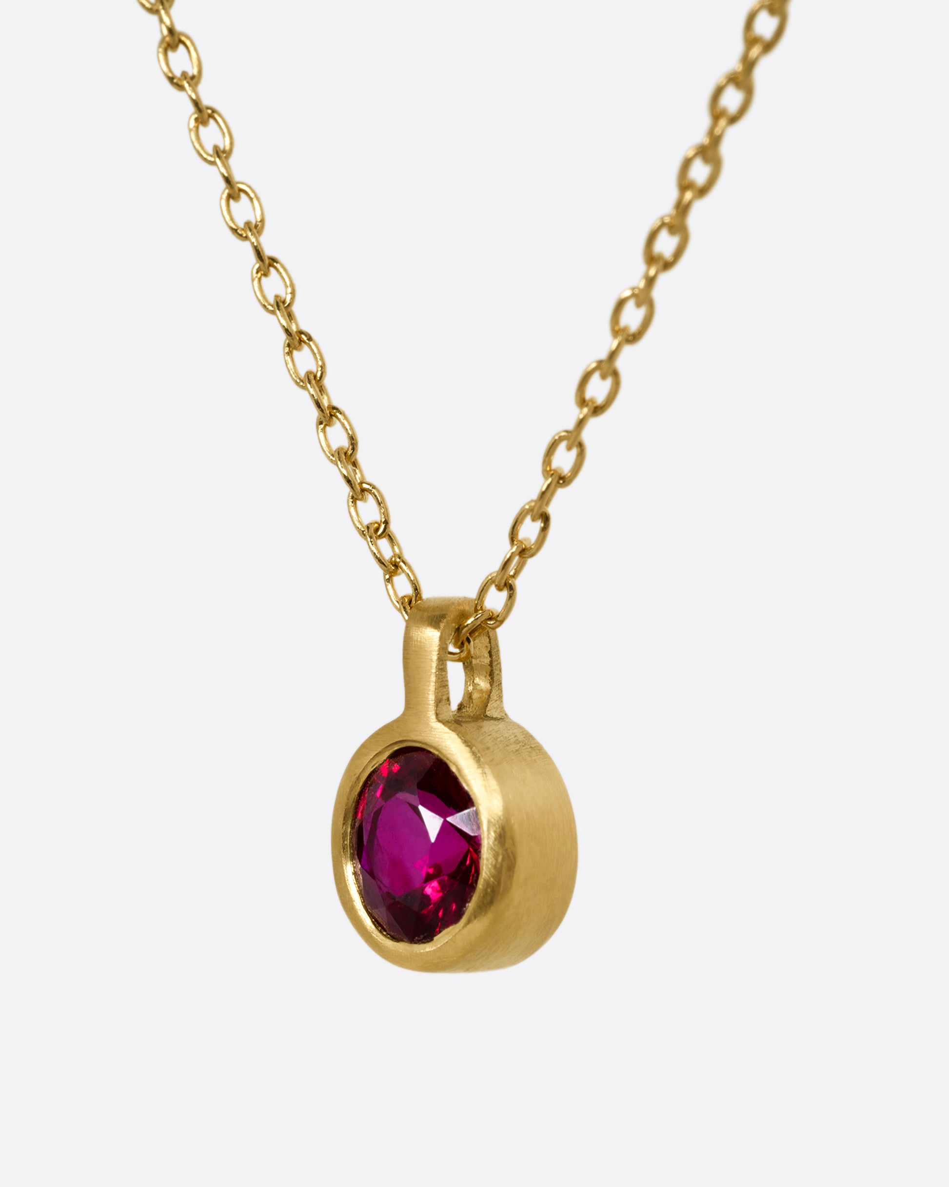 A yellow gold cable chain necklace with a single round ruby in a brushed gold bezel. Shown from the side.