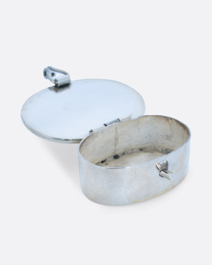 An oval alpaca silver box with a closure in front. Shown open at an angle from the front.