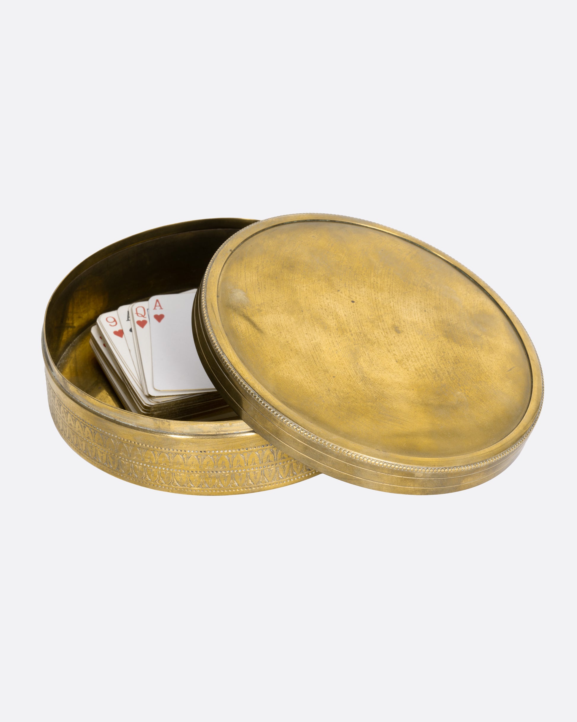 A circular brass box with a lid, shown with a deck of cards in it, with the lid tilted on its side.