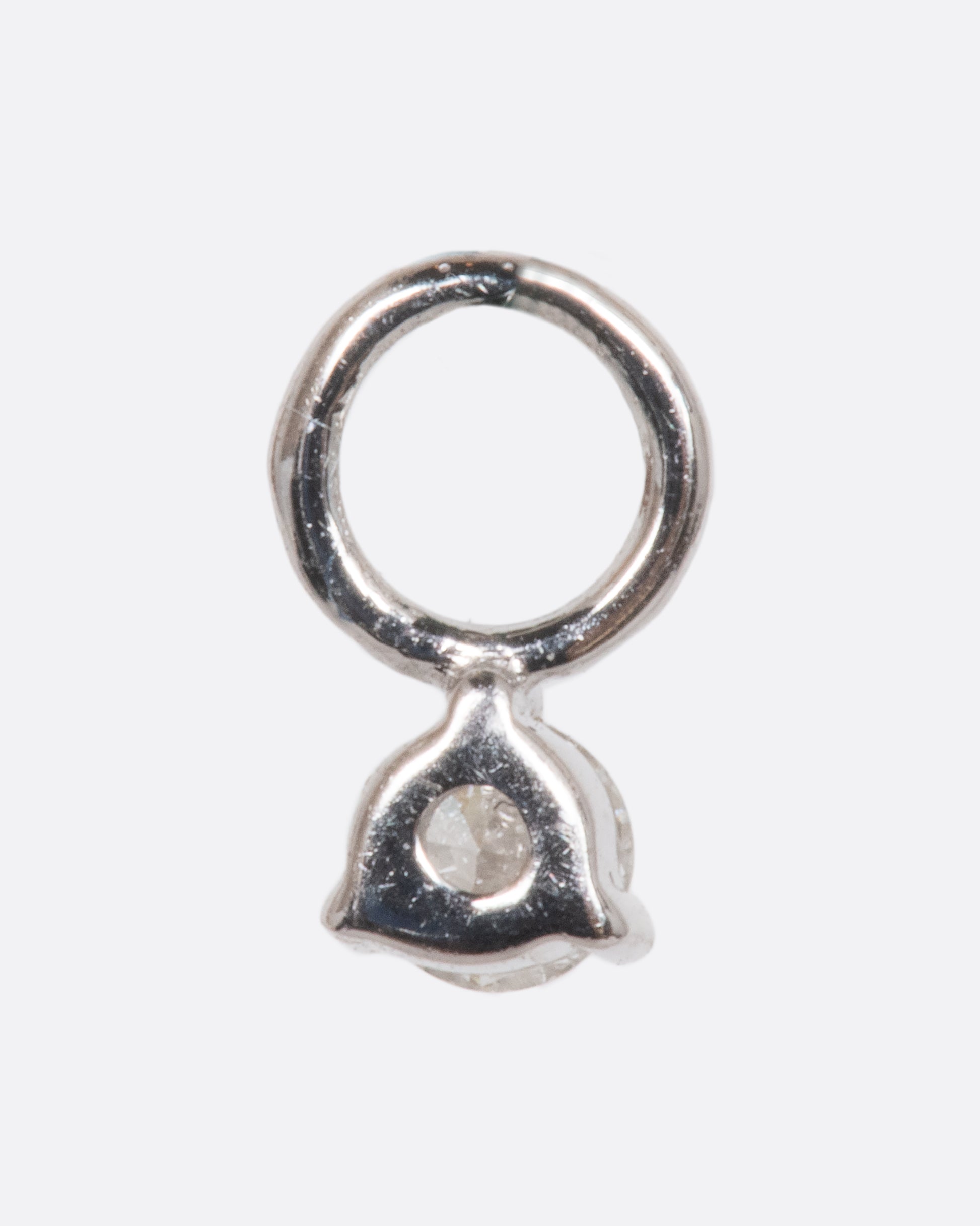 A dangle with a white gold prong setting and jump ring and a white diamond. Shown from the back.
