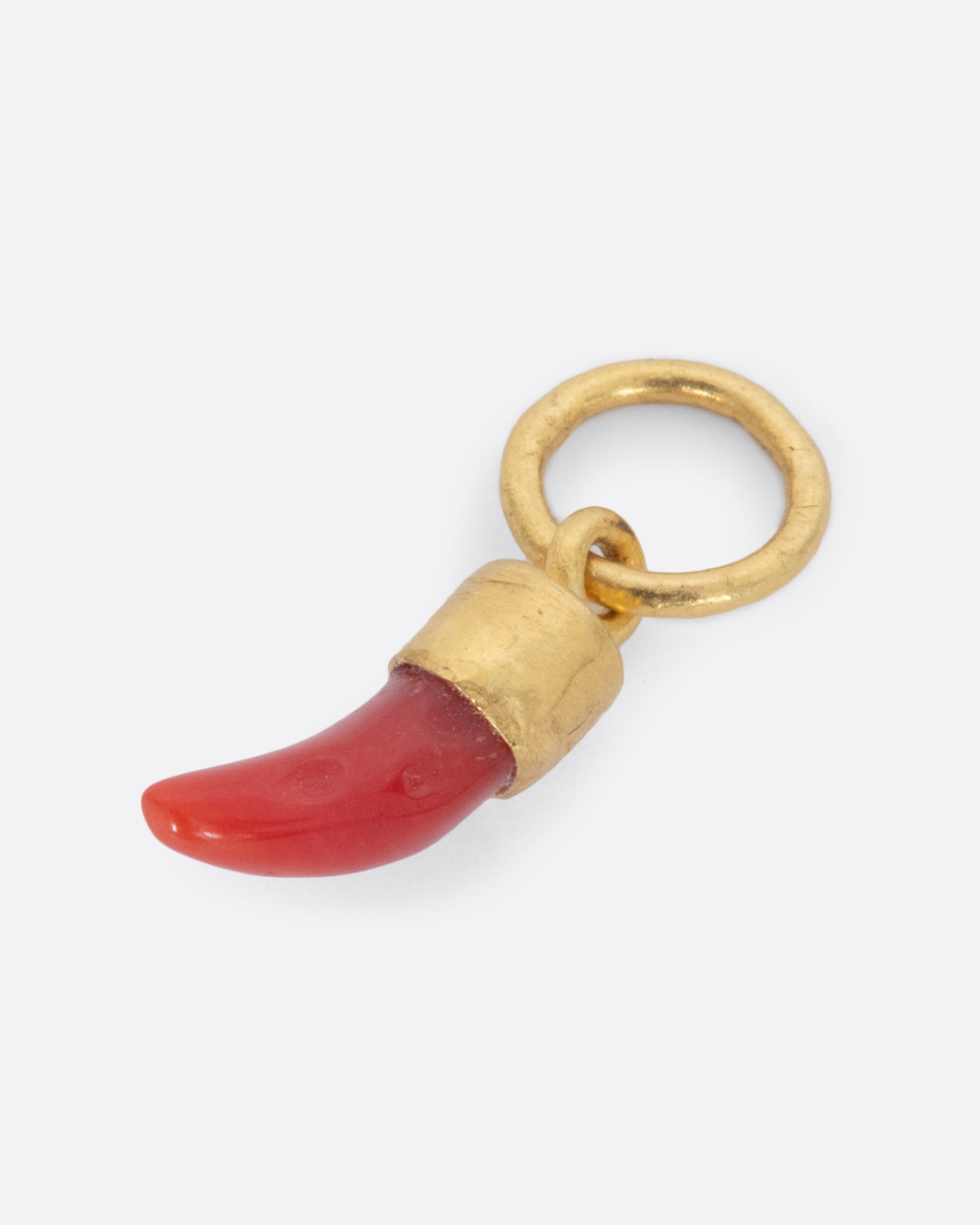 A coral Italian horn dangle with a yellow gold bail and jump ring. Shown lying flat from the side.