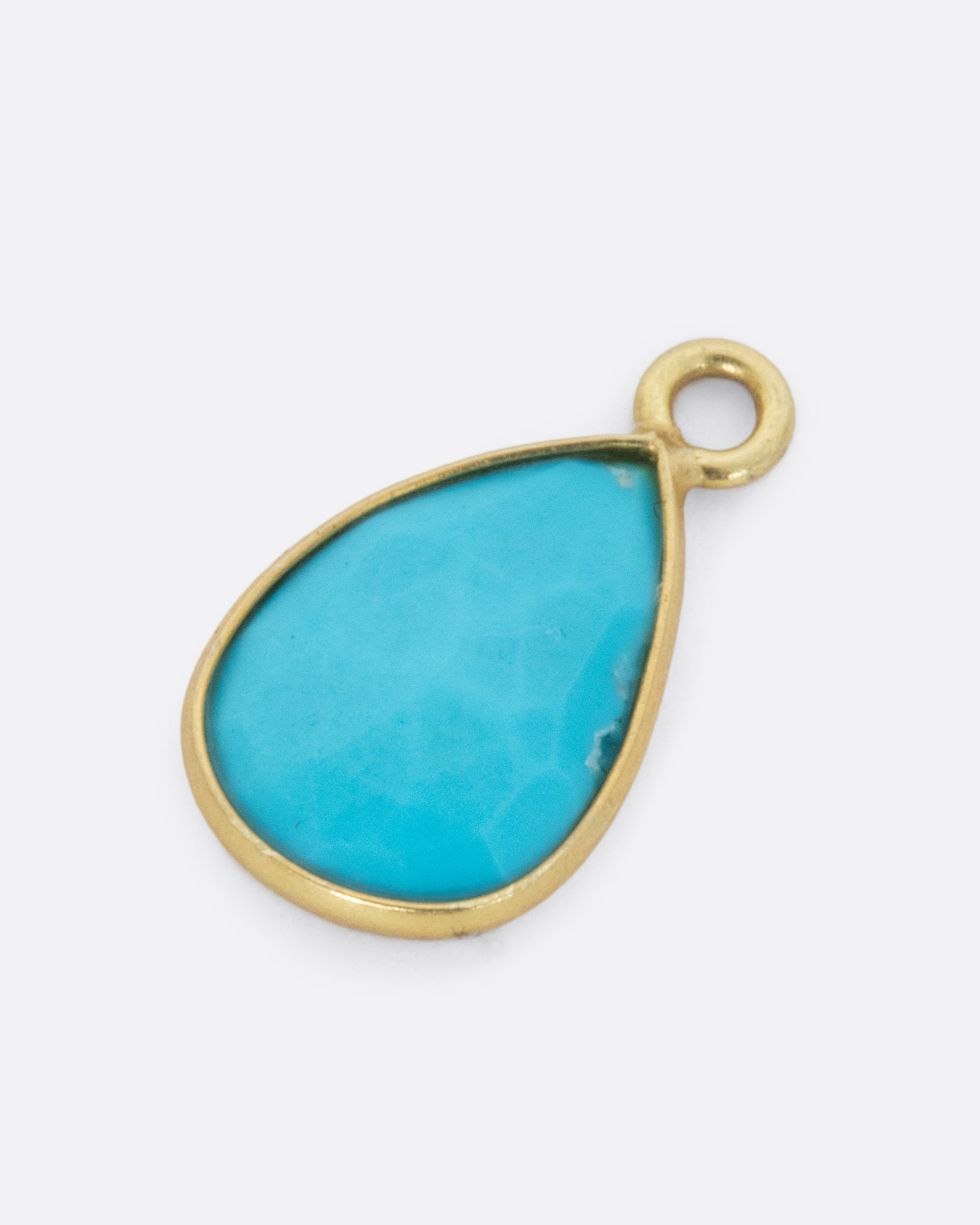 A turquoise teardrop shaped dangle set in yellow gold with a yellow gold bail. Shown diagonally lying flat from the front.