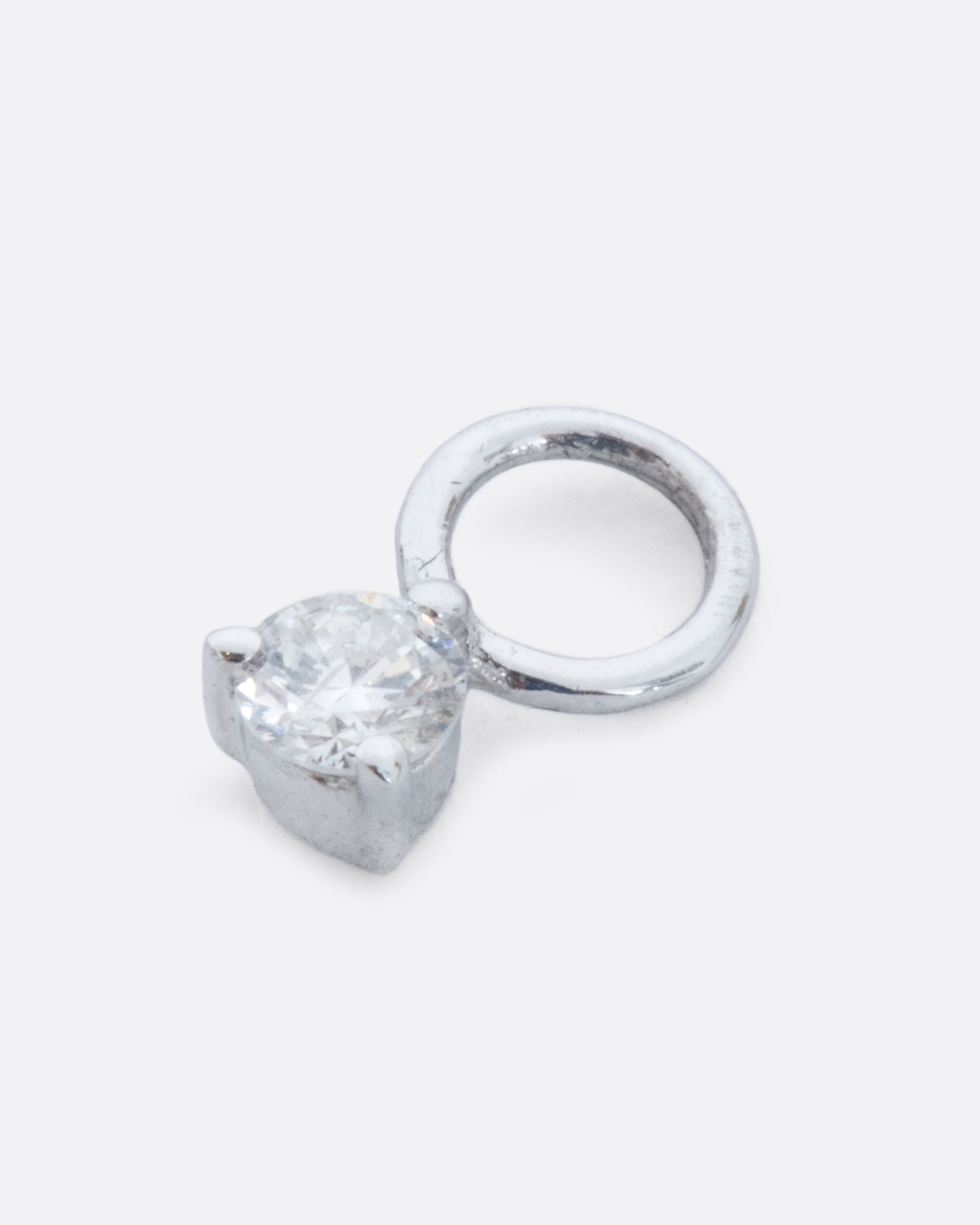 A dangle with a white gold prong setting and jump ring and a white diamond. Shown diagonally lying flat from the front.