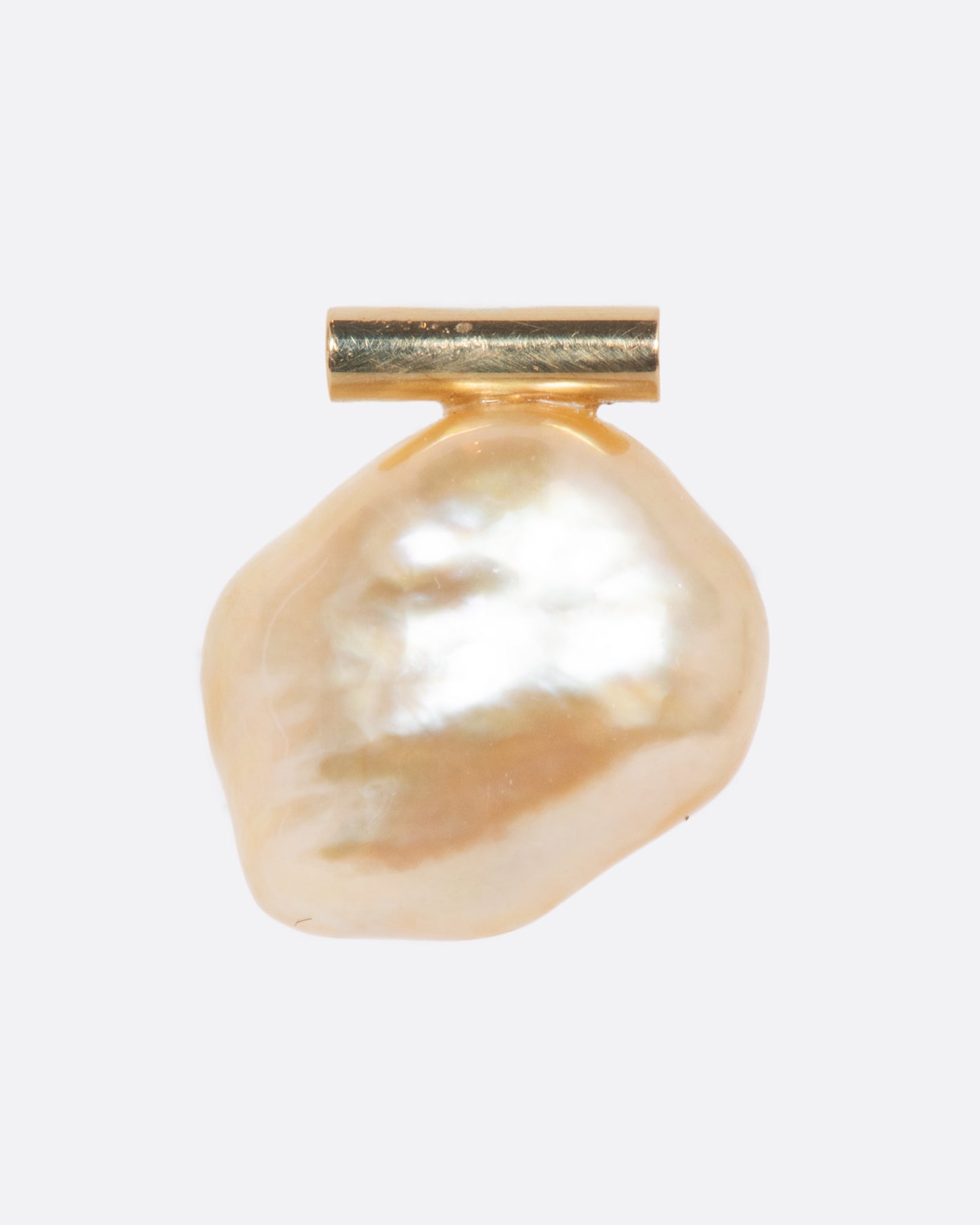 A freeform South Sea baroque pearl is suspended from a modern gold bar setting. The organic curvature of this rare pearl allows light to reflect in all directions, creating radiance from every angle... A sleek yet natural piece. View from the front.