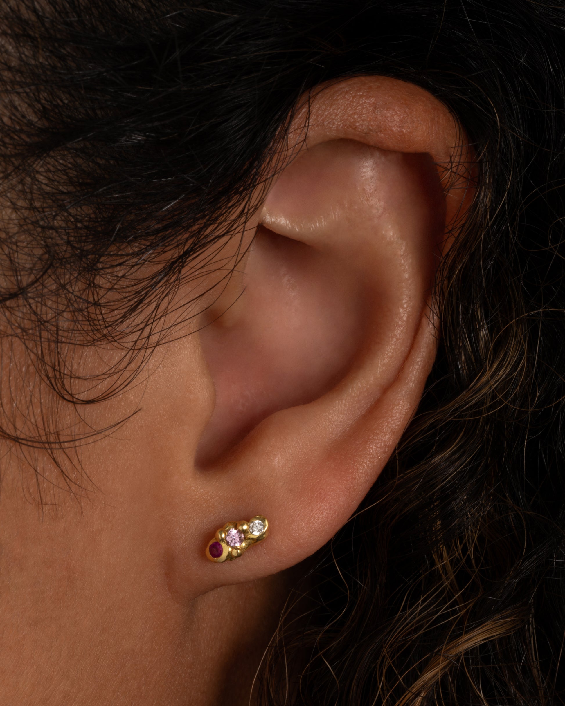 A pair of yellow gold bubble studs with diamonds, sapphires and rubies. Shown worn in an ear.