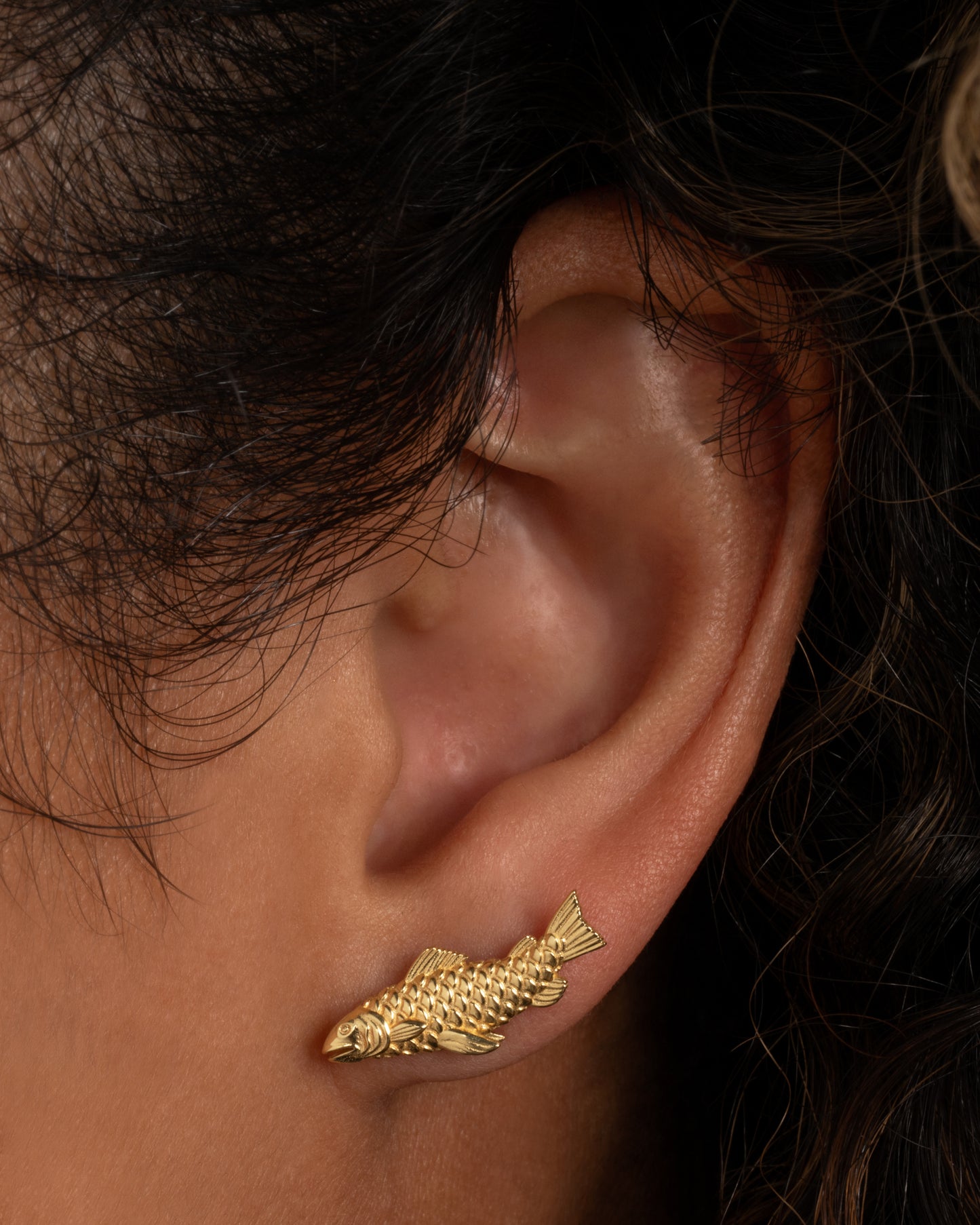 A yellow gold fish earring. Shown from the front on a person.
