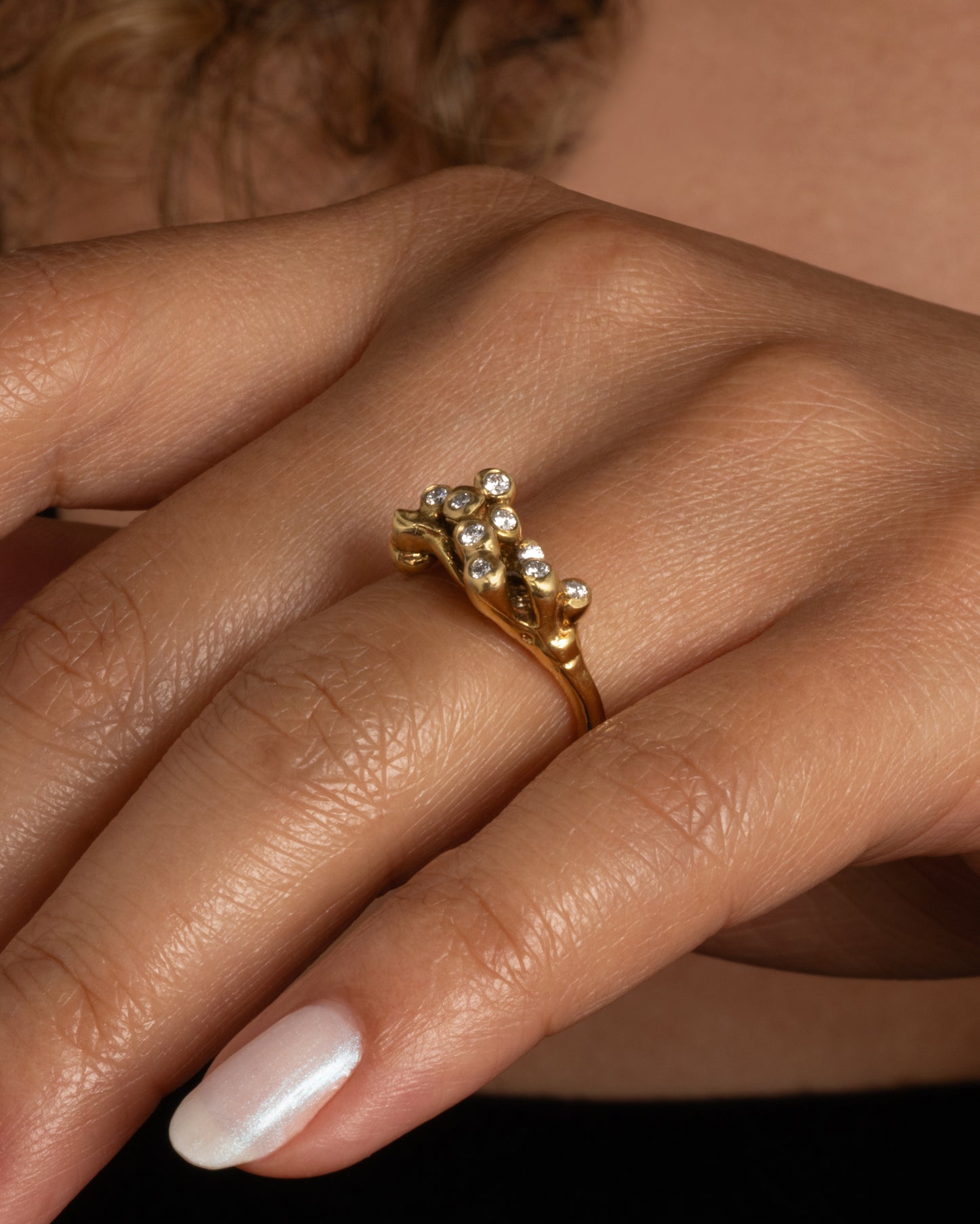 A yellow gold ring with diamond tipped anemones. Shown from the side on a hand.