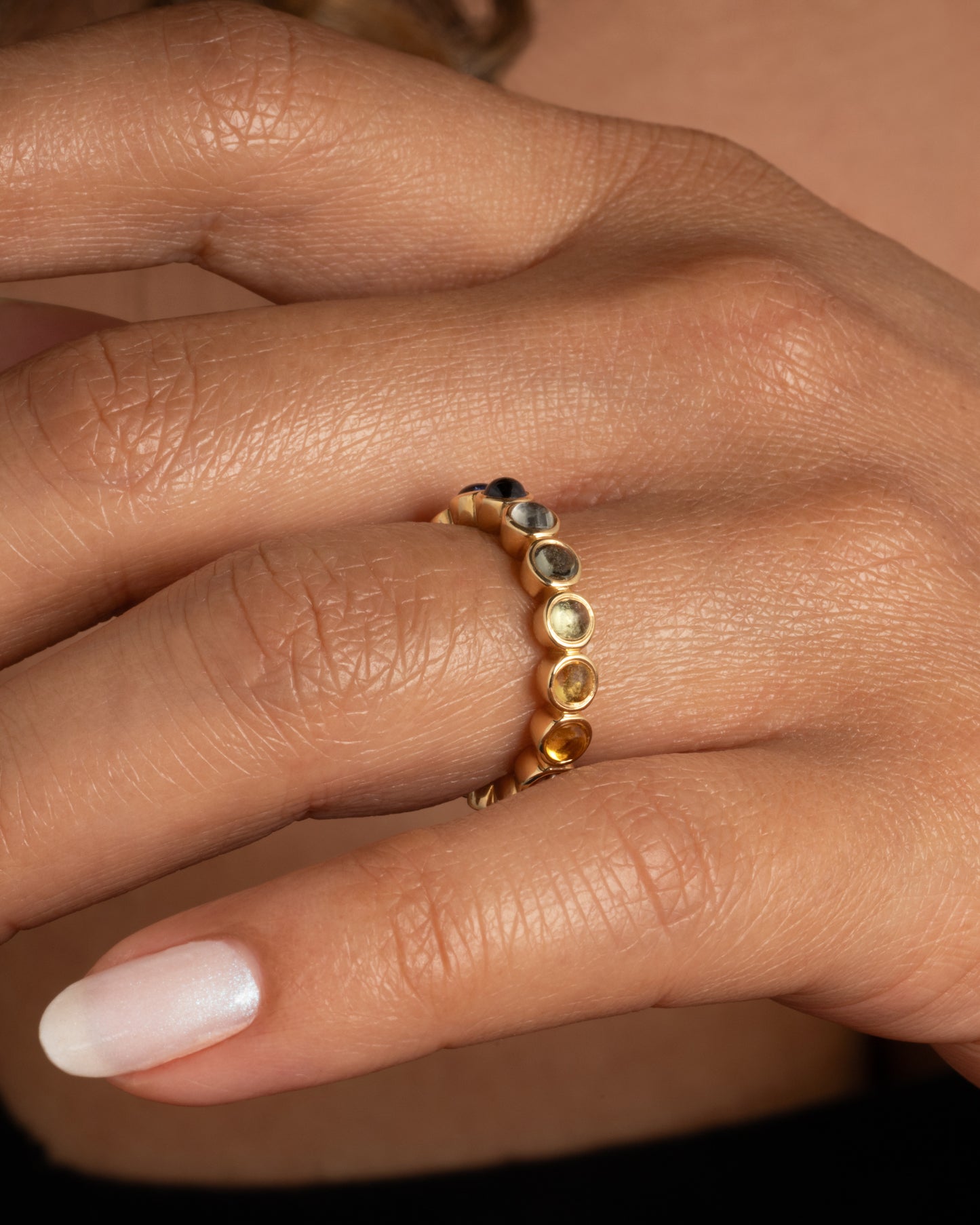 A yellow gold half eternity band with multicolor bezel set sapphire cabochons. Shown worn on a finger.