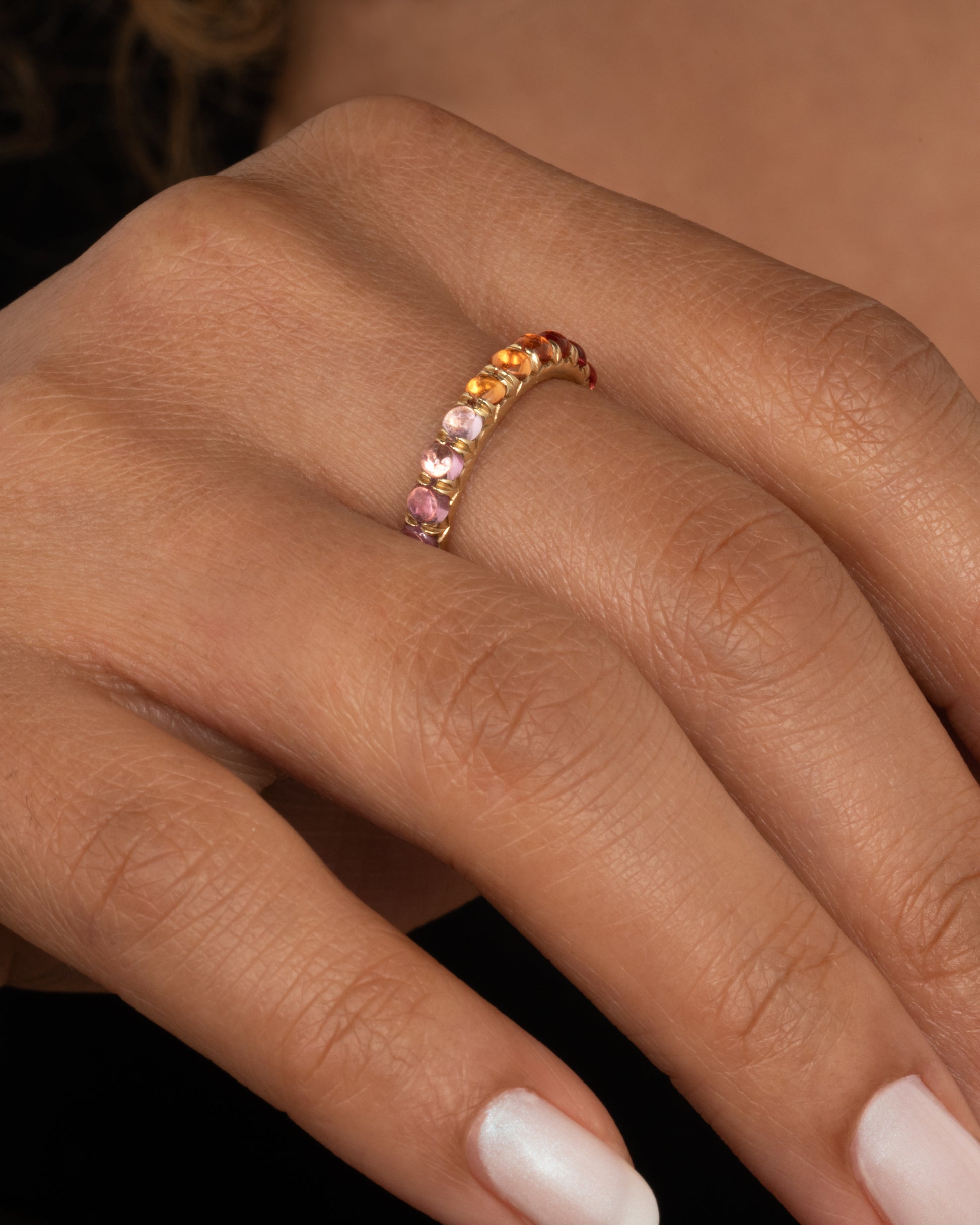 A yellow gold eternity band with rainbow sapphire cabochons. Shown worn on a finger.