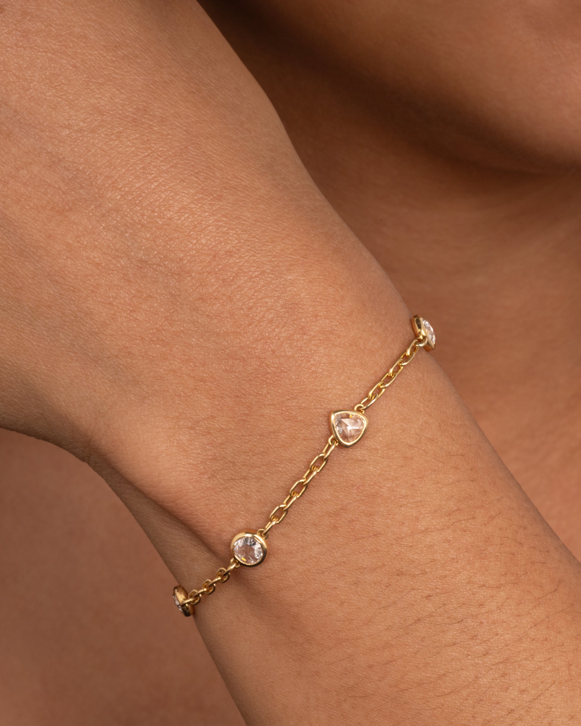 A yellow gold cable chain bracelet with four bezel set diamonds. Shown worn around a wrist.