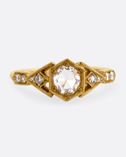 A yellow gold ring with a center diamond and angular side cutouts and diamond accents. Shown from the front.