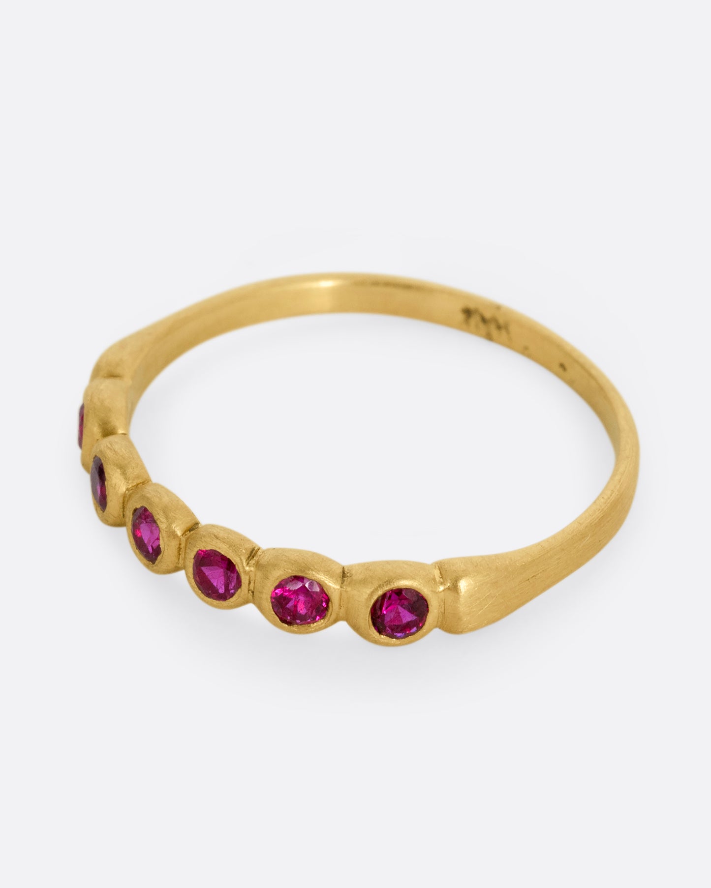 A yellow gold ring with six bezel set rubies. Shown from the side.