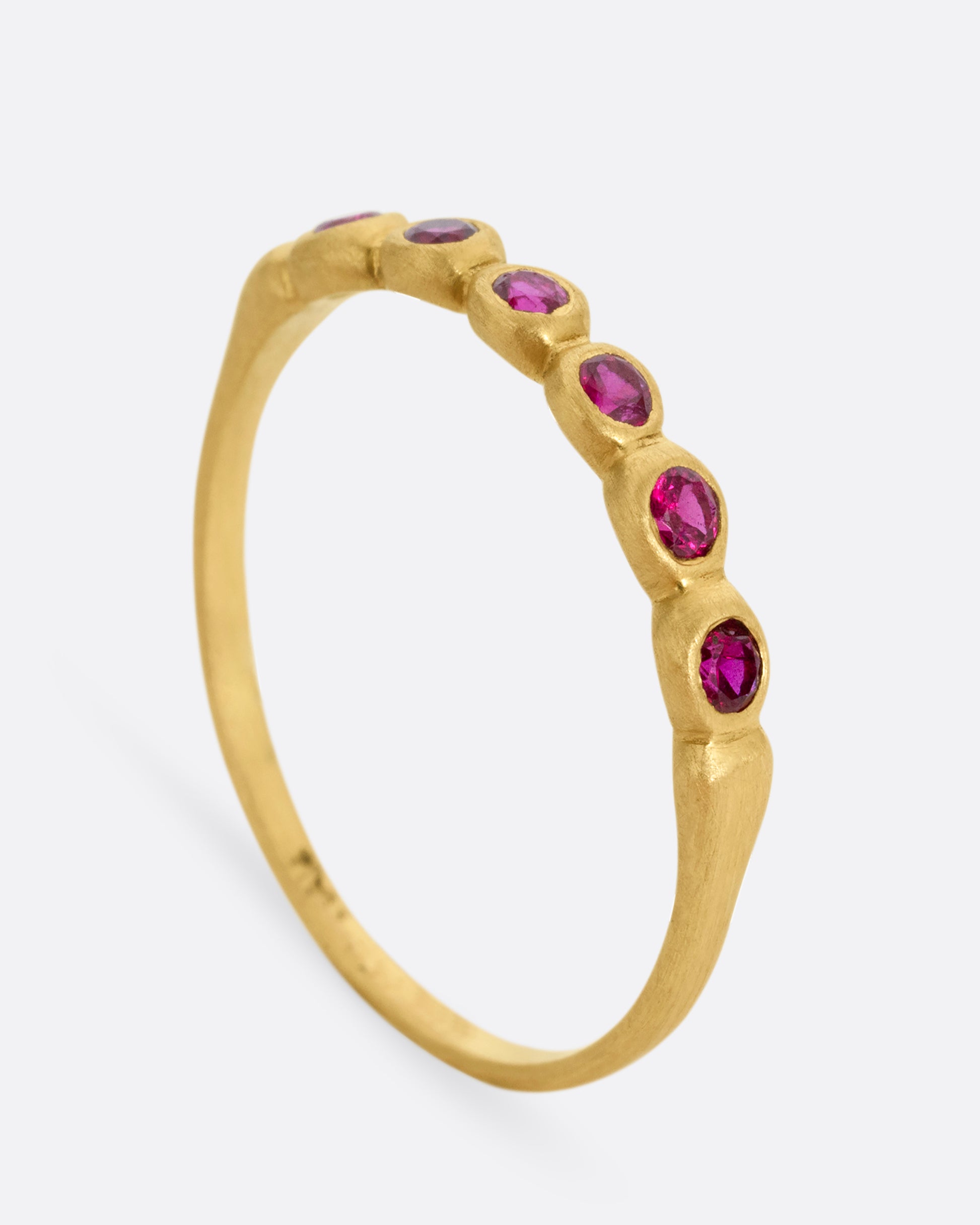 A yellow gold ring with six bezel set rubies. Shown standing up from the side.