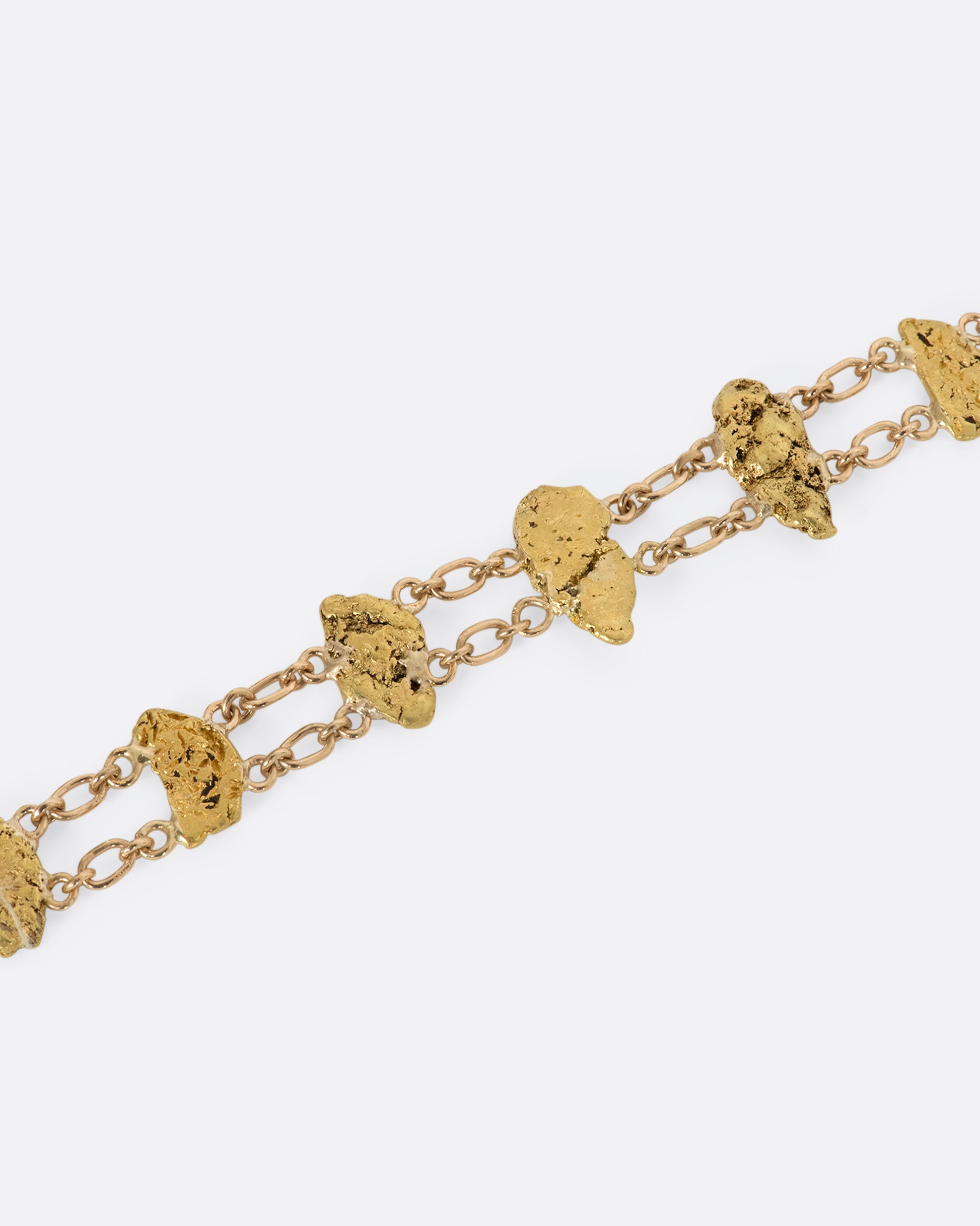 A yellow gold nugget bracelet featuring nine solid nuggets. View of nuggets and chain close up.