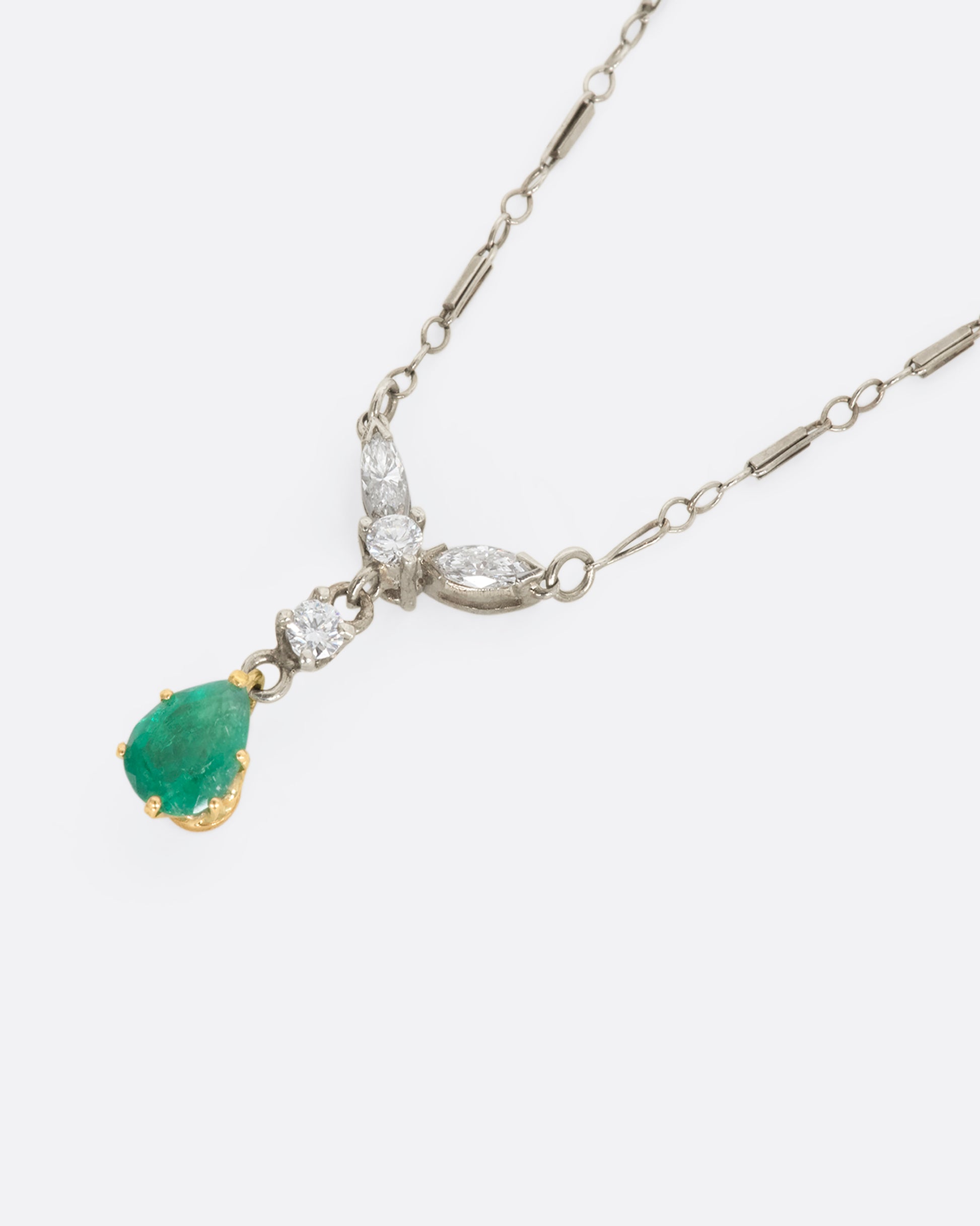 White gold necklace featuring diamonds and an emerald at the center. View close up lying flat, from the side.