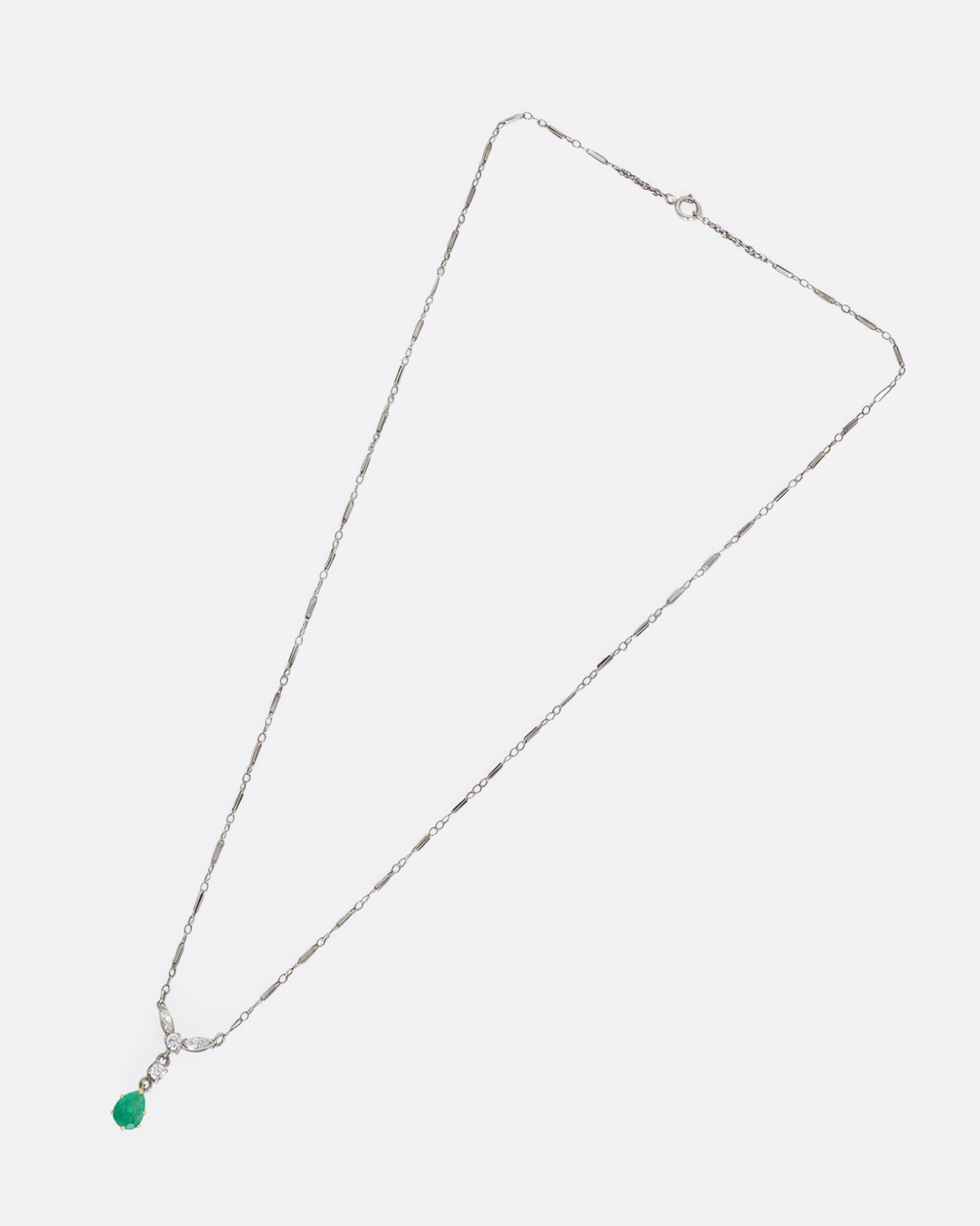 White gold necklace featuring diamonds and an emerald at the center. View from above, lying flat.