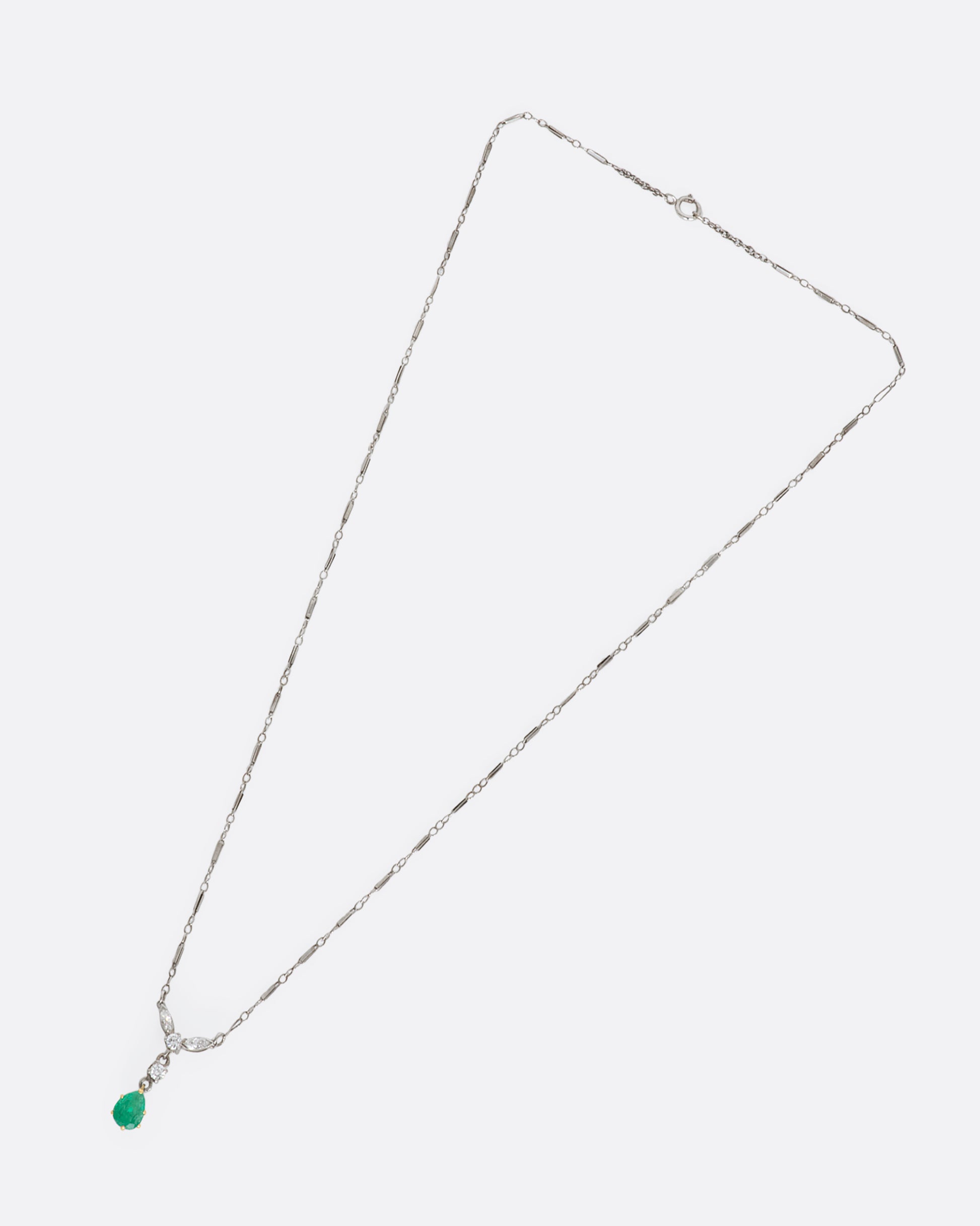 White gold necklace featuring diamonds and an emerald at the center. View from above, lying flat.