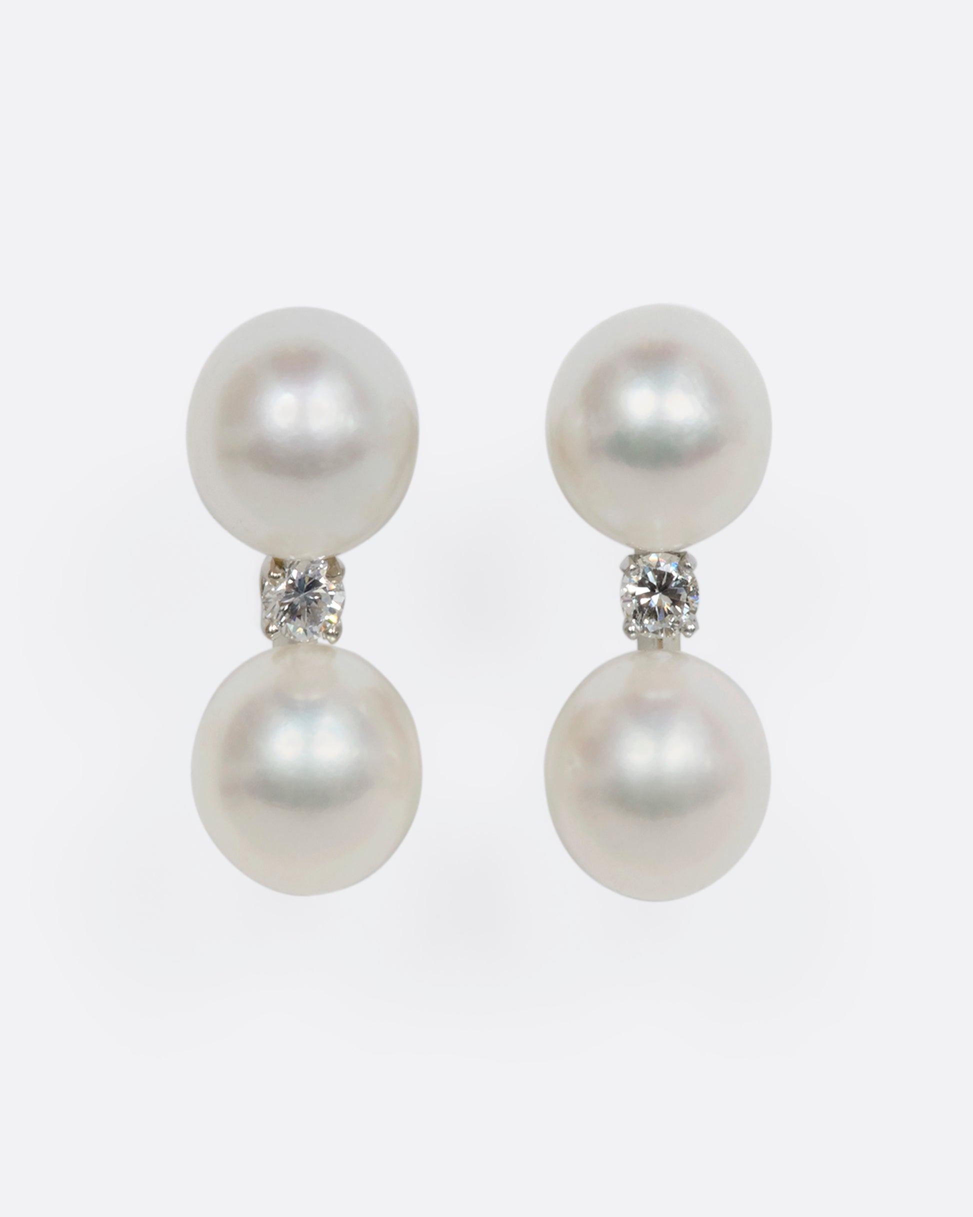 A pair of white gold studs featuring two pearls with a diamond situated in between. View from the front.