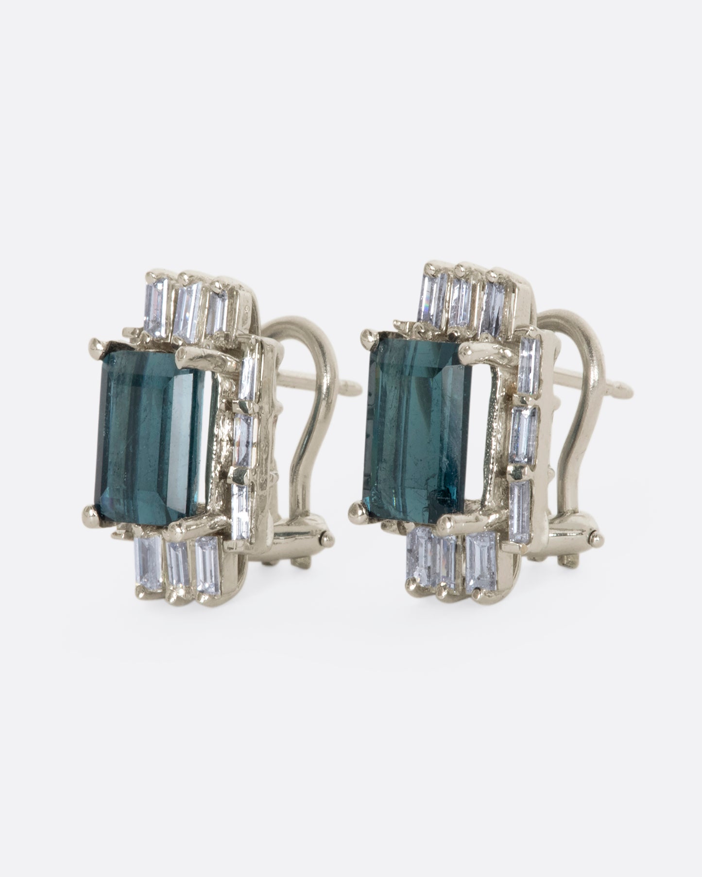 A pair of white gold earrings with emerald cut green tourmalines surrounded by baguette diamonds. View from the side.