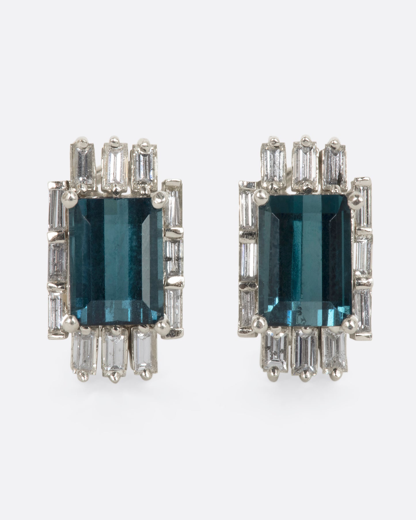 A pair of white gold earrings with emerald cut green tourmalines surrounded by baguette diamonds. View from the front.