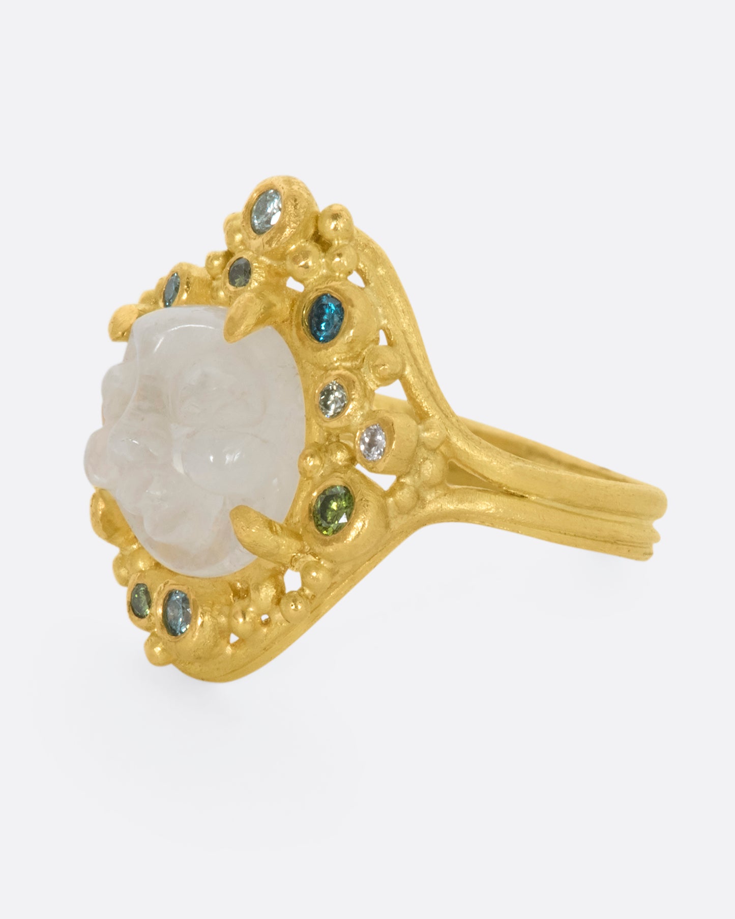 A yellow gold ring featuring a carved moonstone face with a halo of multicolored diamonds. View from the left side.