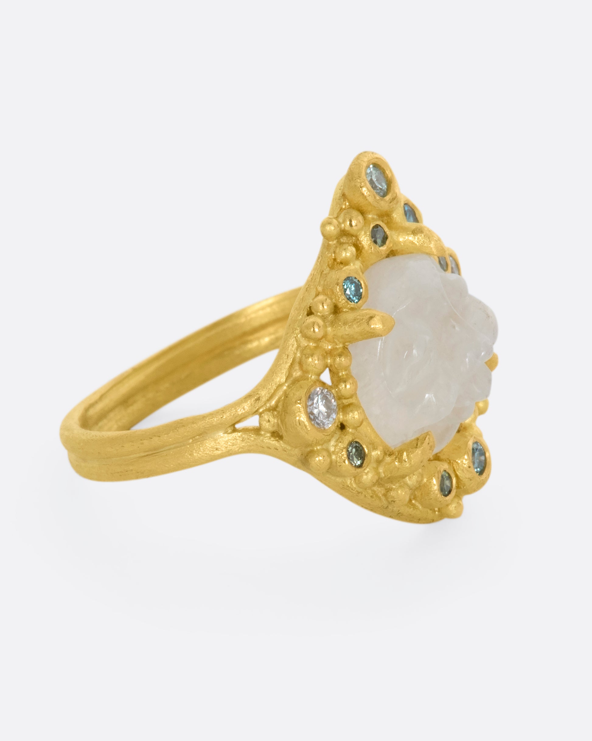 A yellow gold ring featuring a carved moonstone face with a halo of multicolored diamonds. View from the right side.