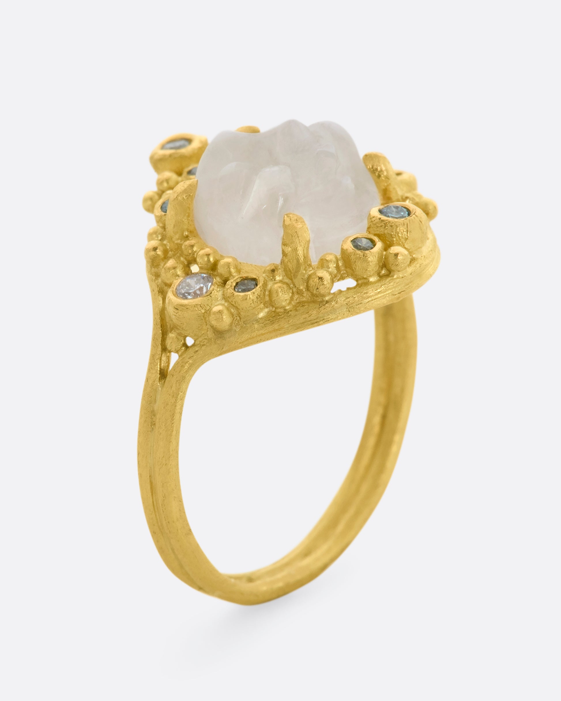 A yellow gold ring featuring a carved moonstone face with a halo of multicolored diamonds. View standing.