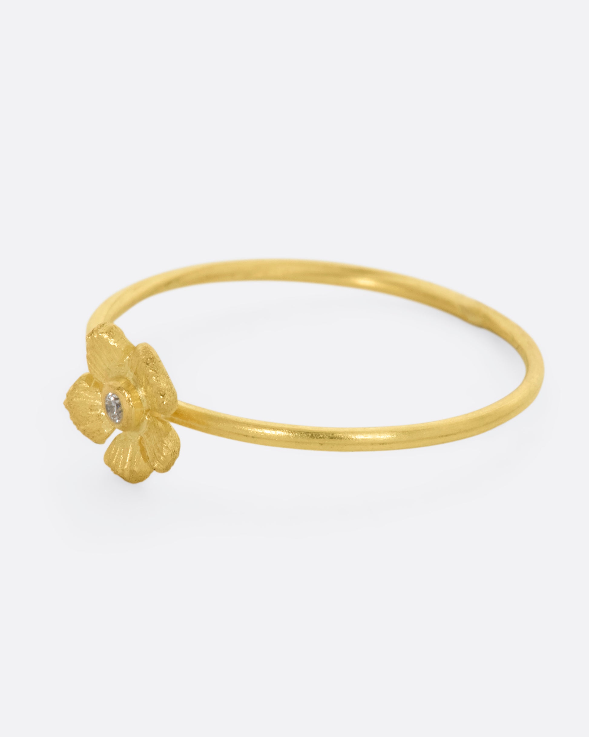 A small yellow gold flower with diamond at the center on a dainty band. View from the left side.