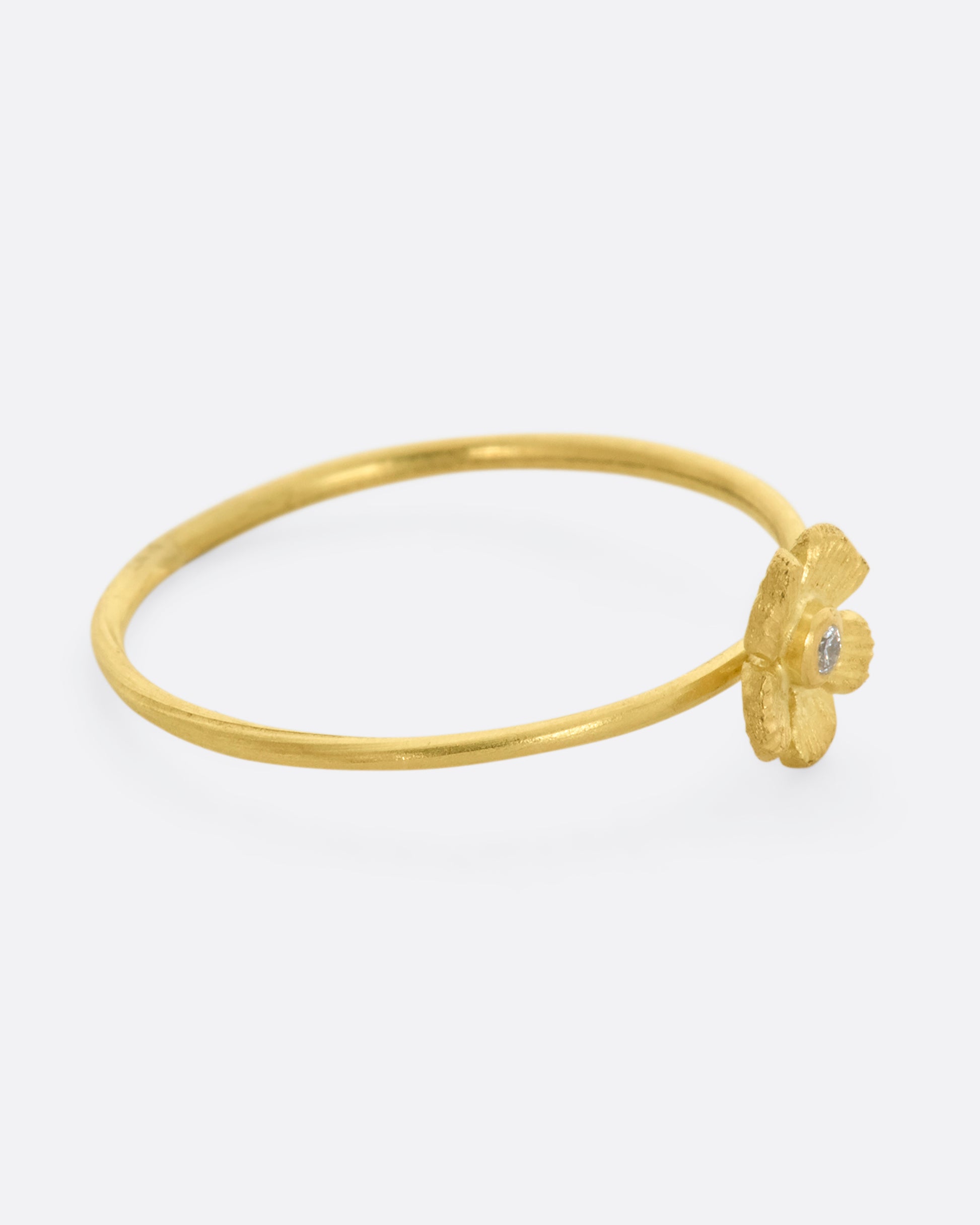 A small yellow gold flower with diamond at the center on a dainty band. View from the right side.