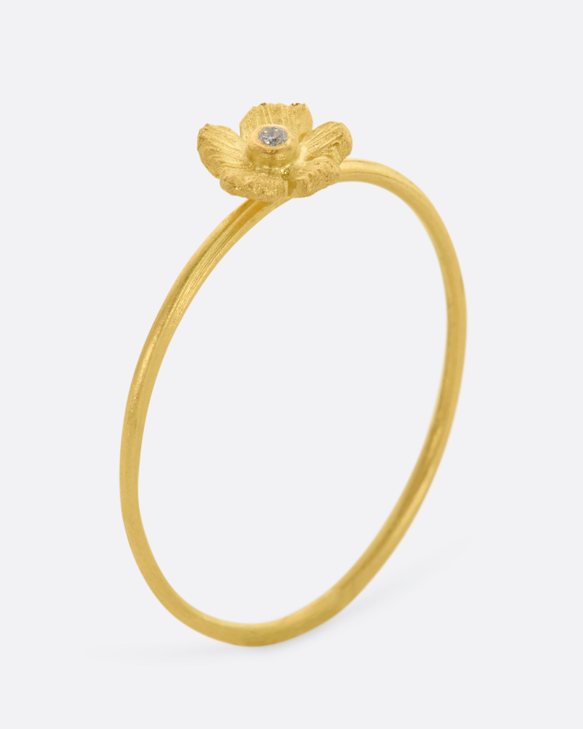 A small yellow gold flower with diamond at the center on a dainty band. View standing up.