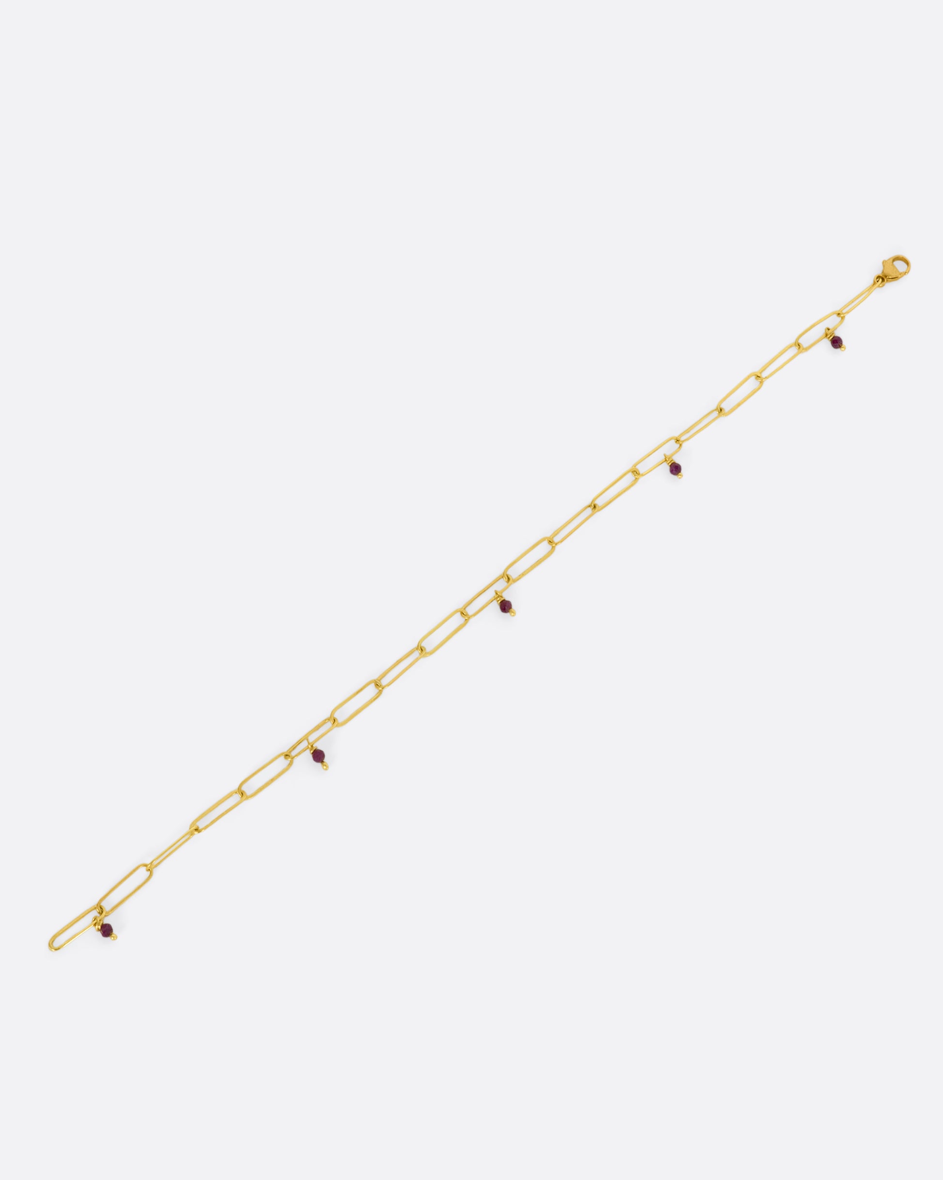 A yellow gold oval link bracelet with 5 tiny raw ruby beads spaced throughout. View lying flat, from above, not closed.