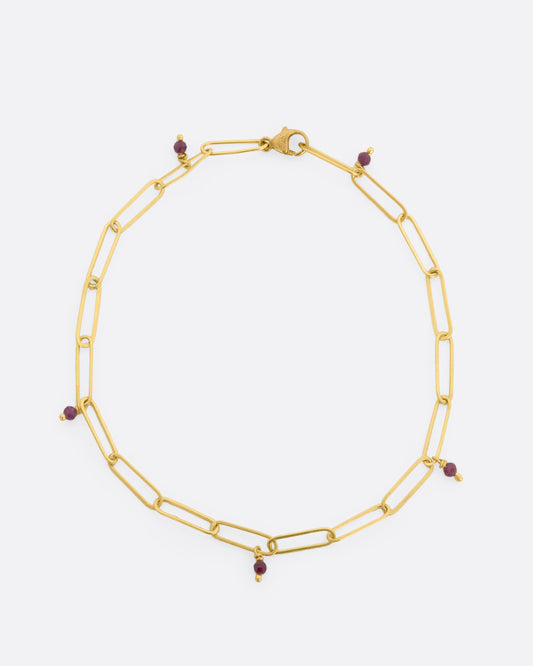 A yellow gold oval link bracelet with 5 tiny raw ruby beads spaced throughout. View lying flat, from above.