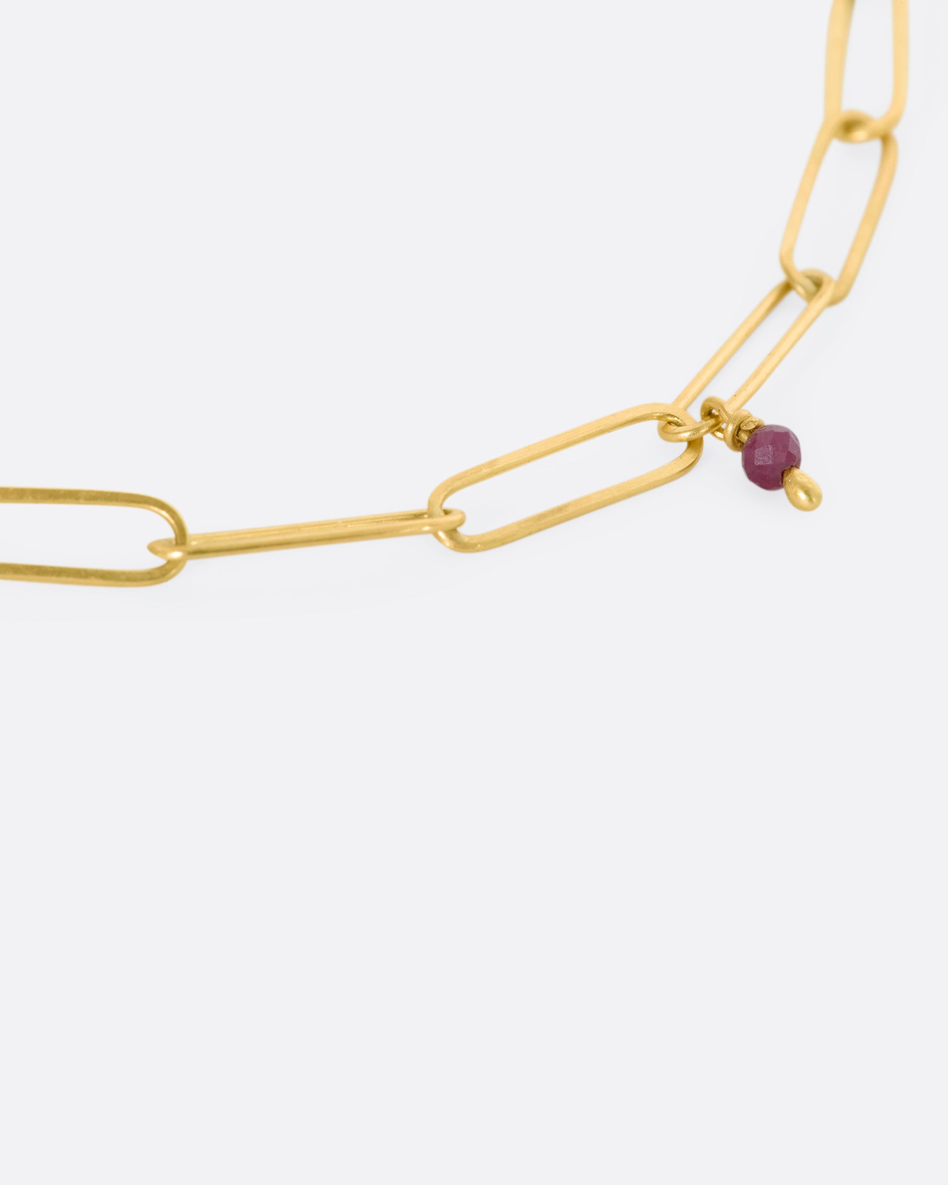 A yellow gold oval link bracelet with 5 tiny raw ruby beads spaced throughout. Close up view of single raw ruby and chain links.