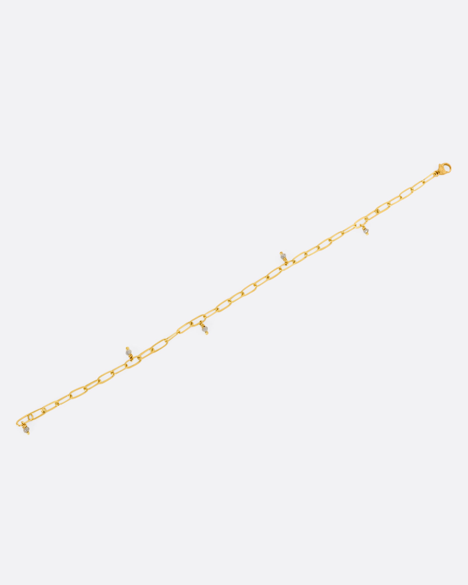 A yellow gold oval link bracelet with 5 tiny raw diamond beads spaced throughout. View lying flat, from above, not closed.