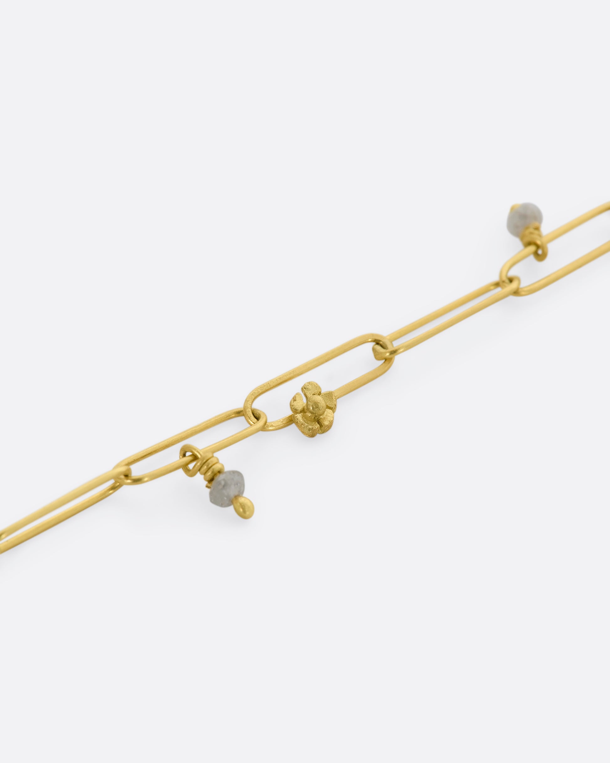 A yellow gold oval link bracelet with tiny raw diamond beads and flowers spaced throughout. View of chain, flower, and bead close up.