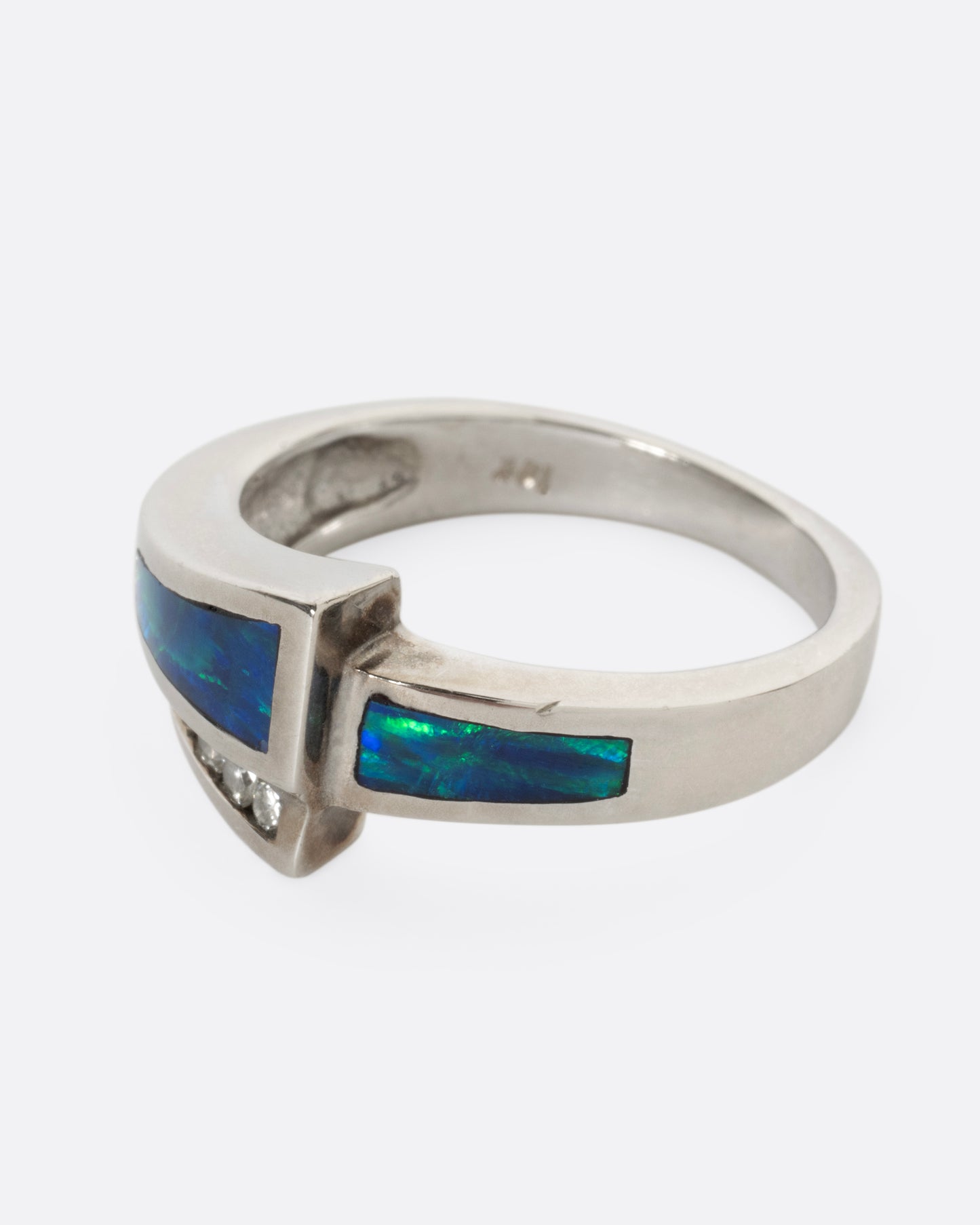 A white gold wrap ring with opal inlay and  a queue of diamonds along the edge, shown from the side.