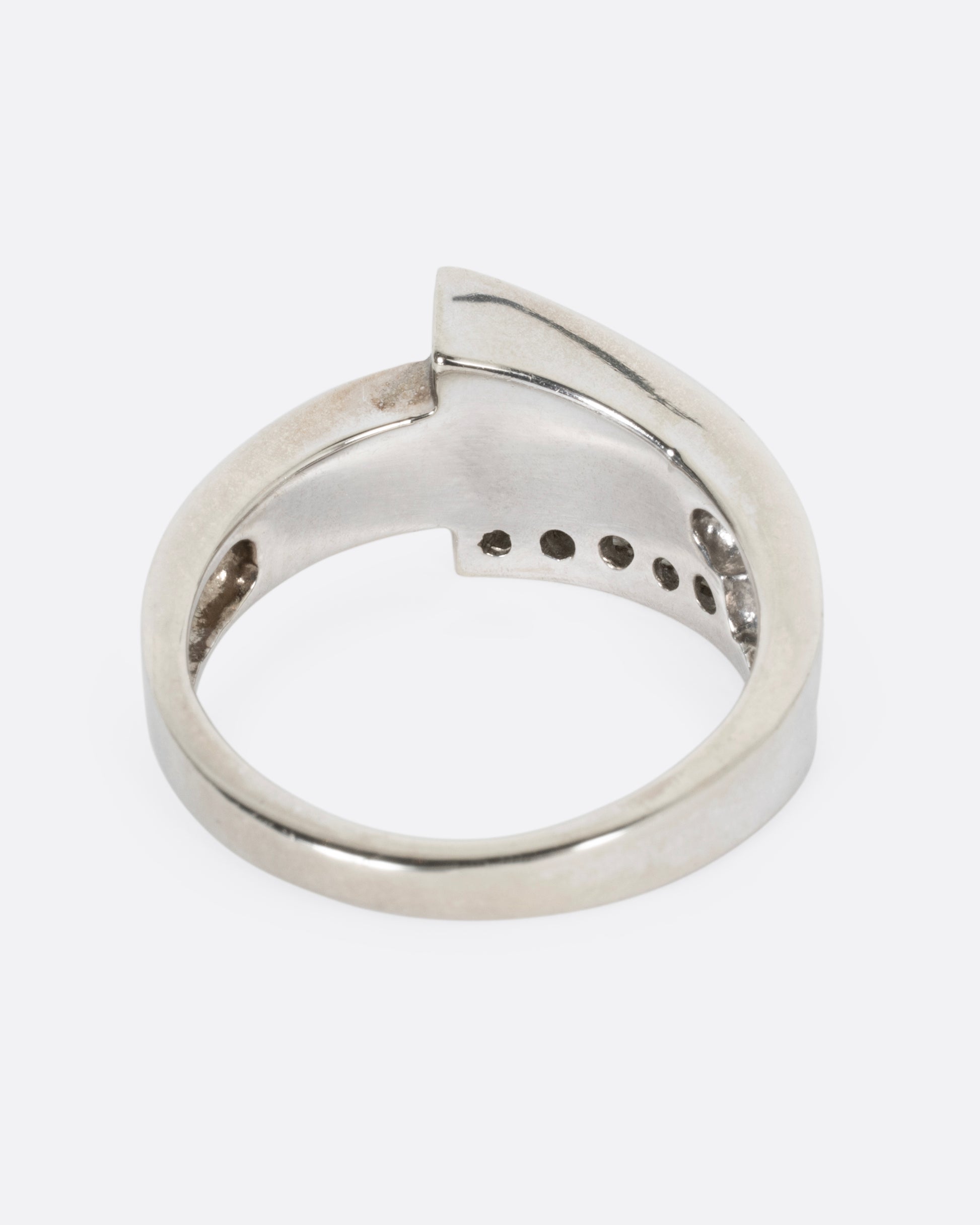 A white gold wrap ring with opal inlay and  a queue of diamonds along the edge, shown from the back.