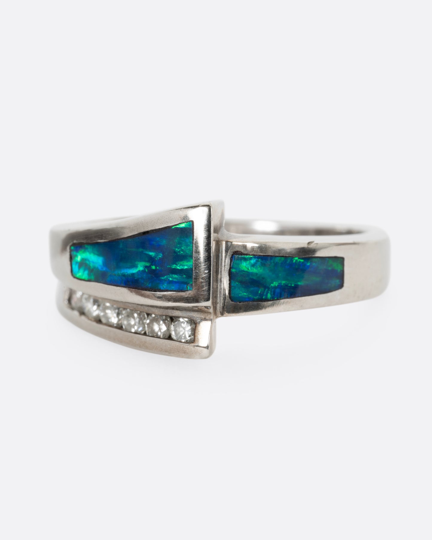 A white gold wrap ring with opal inlay and  a queue of diamonds along the edge, shown from the front.