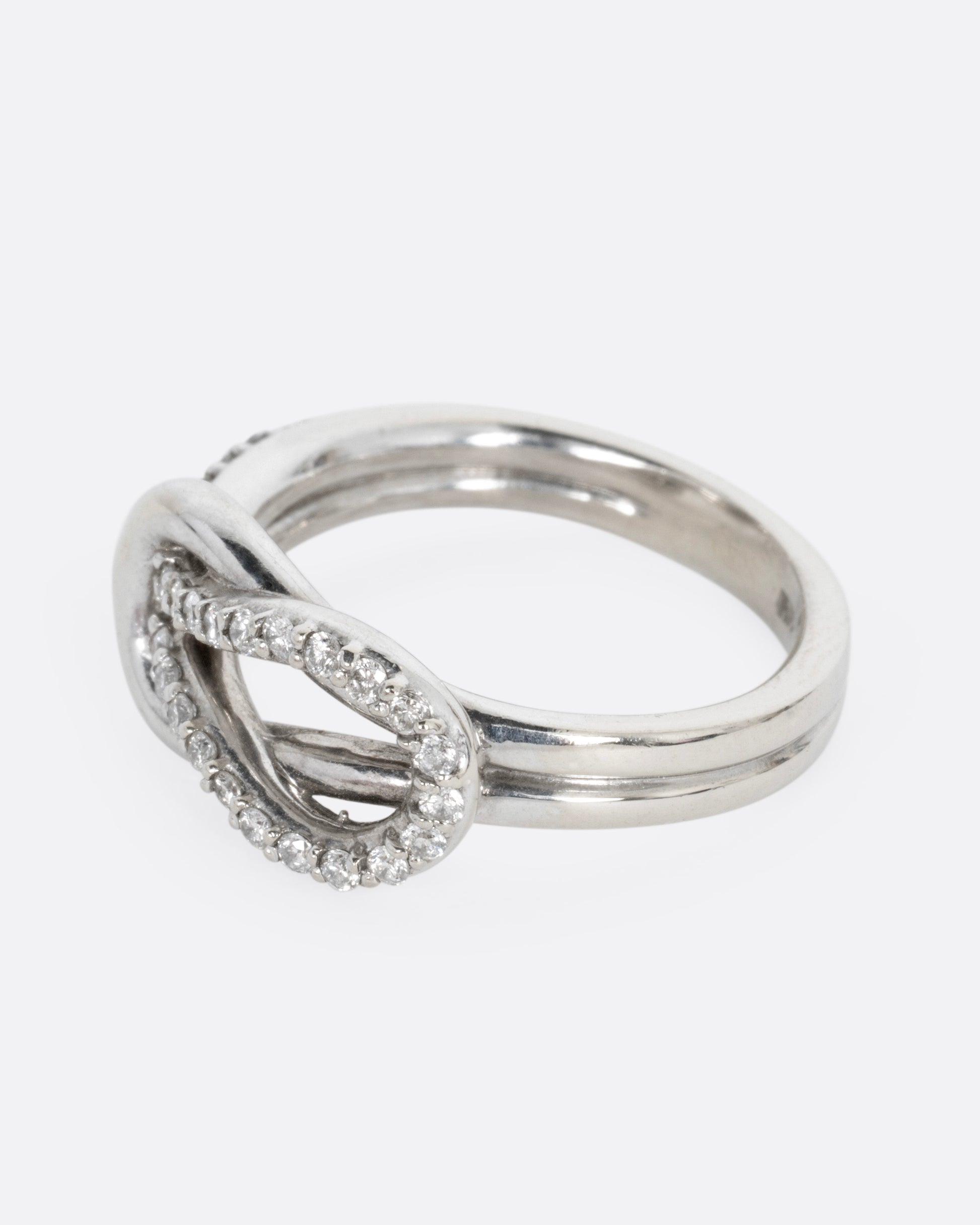 A white gold ring with a diamond studded infinity knot, shown from the side.