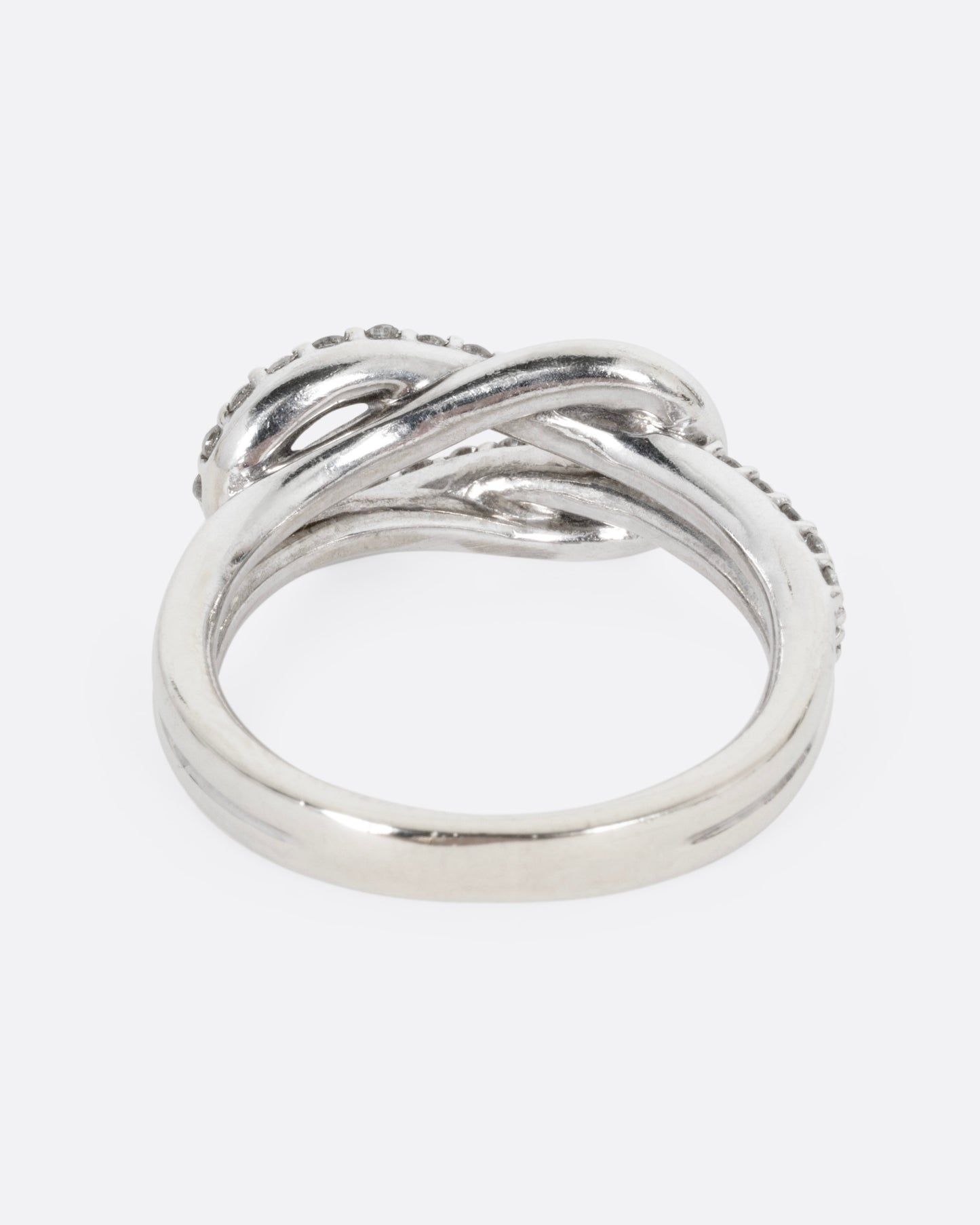 A white gold ring with a diamond studded infinity knot, shown from the back.