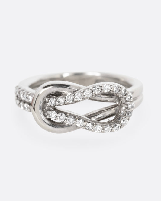 A white gold ring with a diamond studded infinity knot, shown from the front.