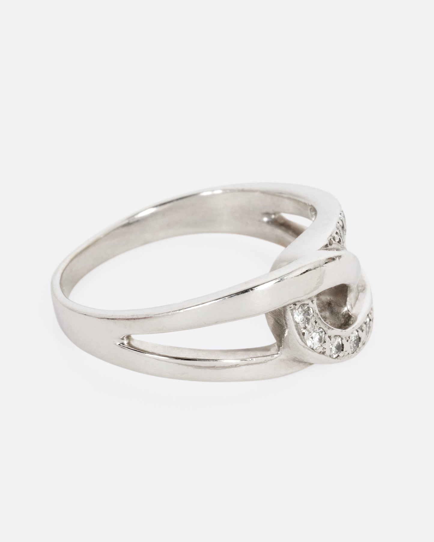 A white gold ring with two interlocking loops; one studded with diamonds, shown from the side.