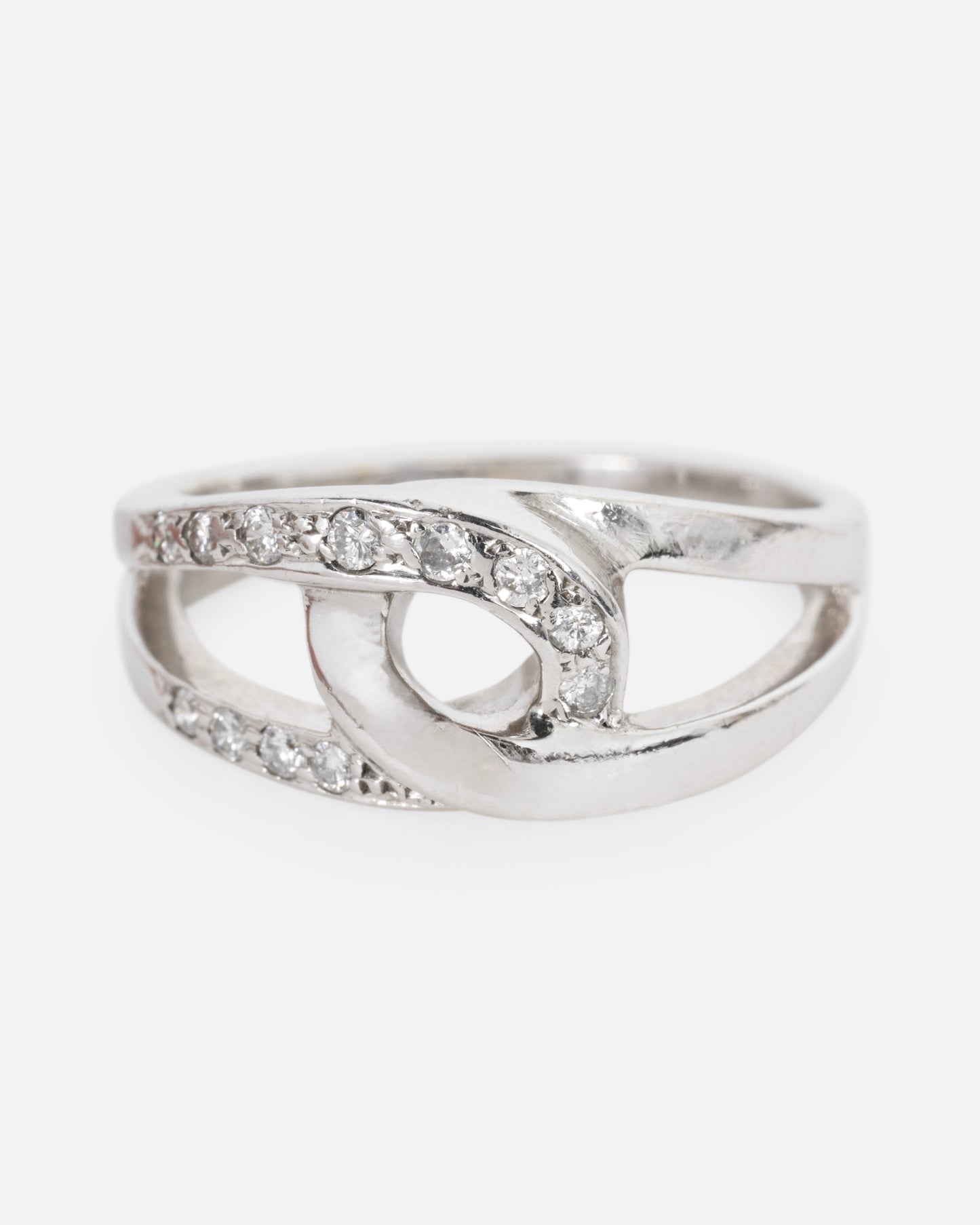 A white gold ring with two interlocking loops; one studded with diamonds, shown from the front.