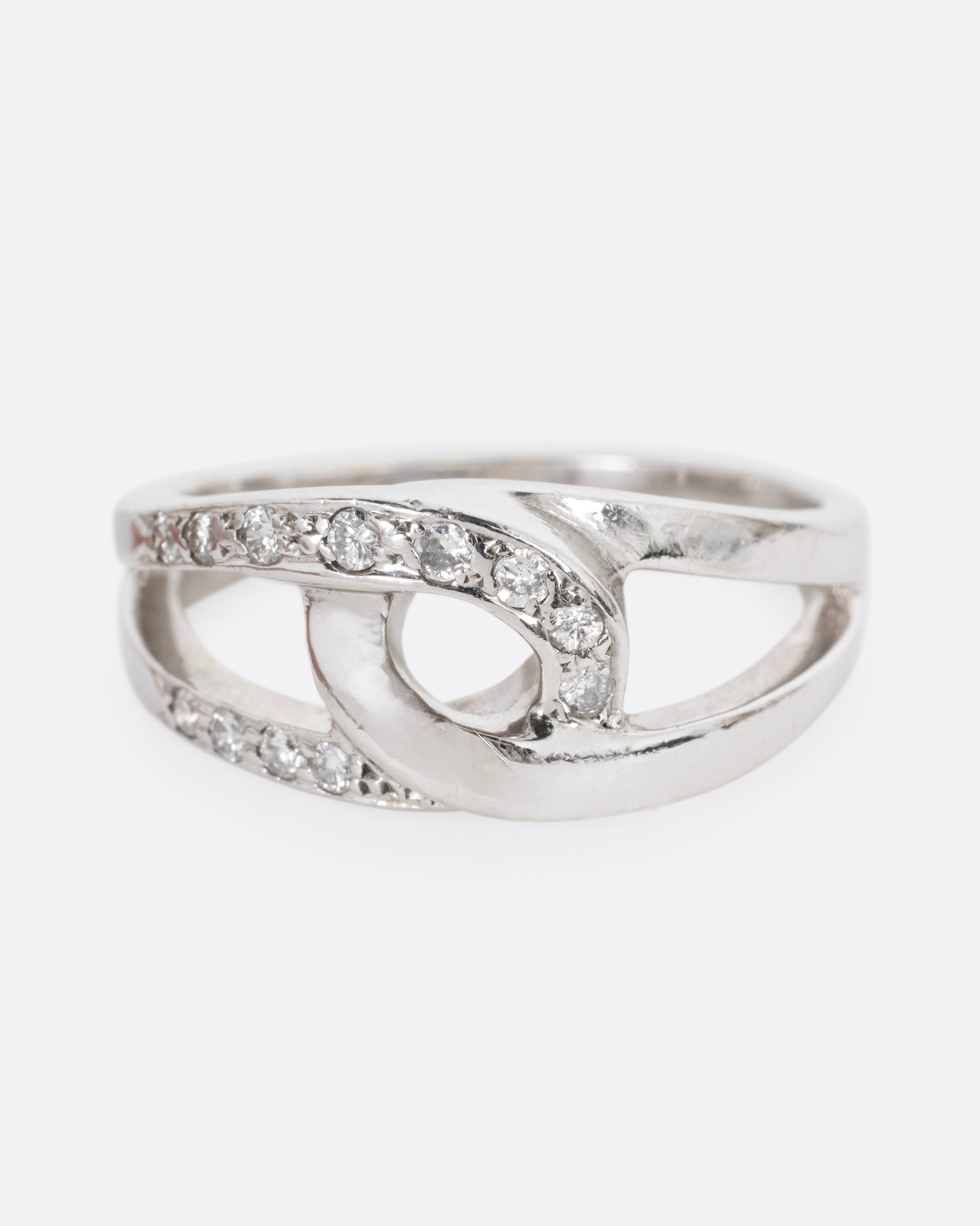 A white gold ring with two interlocking loops; one studded with diamonds, shown from the front.