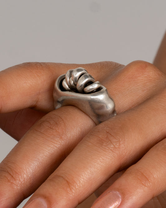 A silver ring with a cluster of free moving hoops nestled into its towering face. Shown from the side on a person.