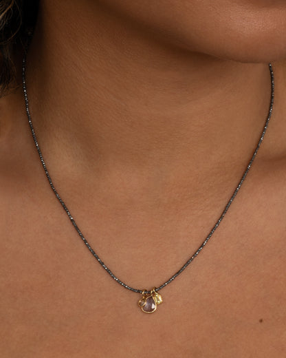 A necklace with oxidized silver Hill Tribe beads and a cluster of blue and green sapphires and a rose cut diamond. Shown from the front on a person.