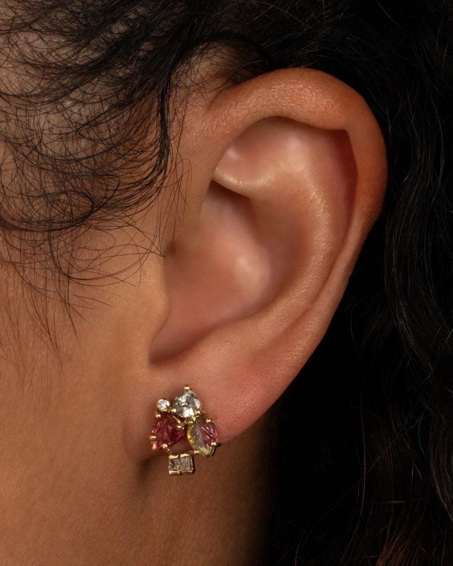A yellow gold stud earring with botanical carved tourmalines and diamond accents. Shown worn in an ear.